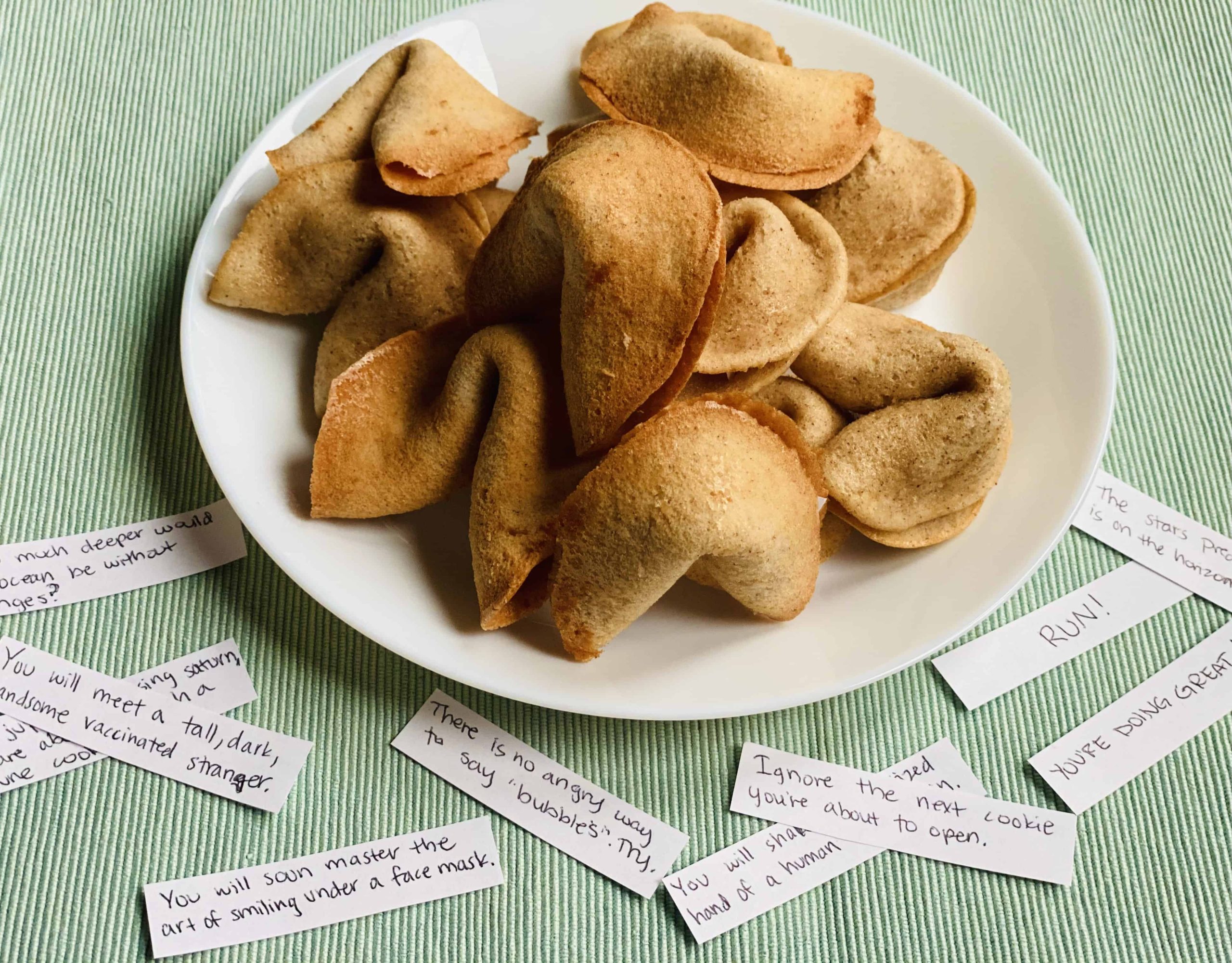 Baked fortune cookies stacked in a pile on a white plate.