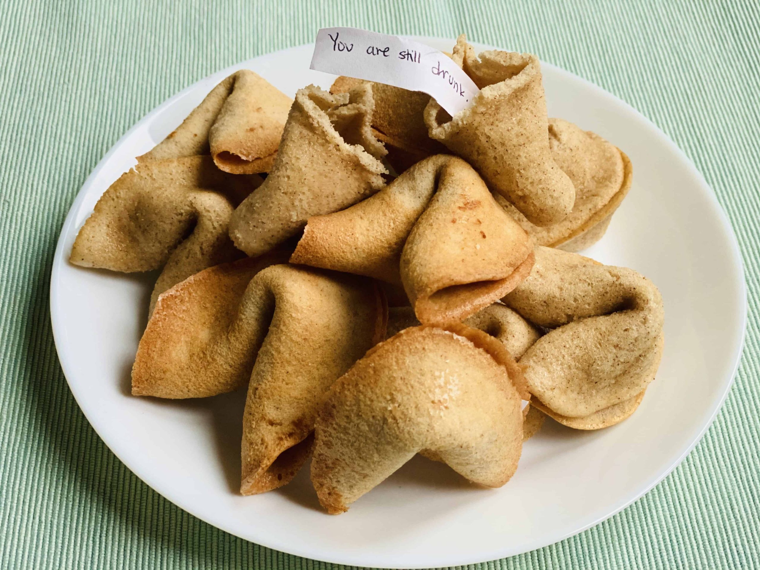 Fortune cookies stacked in a pile on a white plate with a funny fortune message.