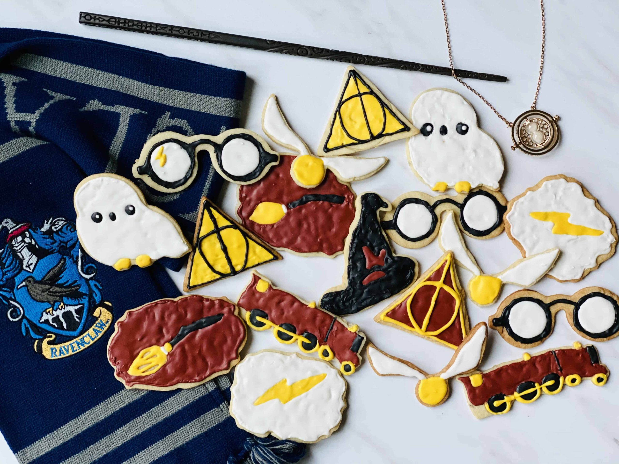Harry Potter sugar cookies laid out on a flat surface next to a wand, a time turner and a Ravenclaw scarf.