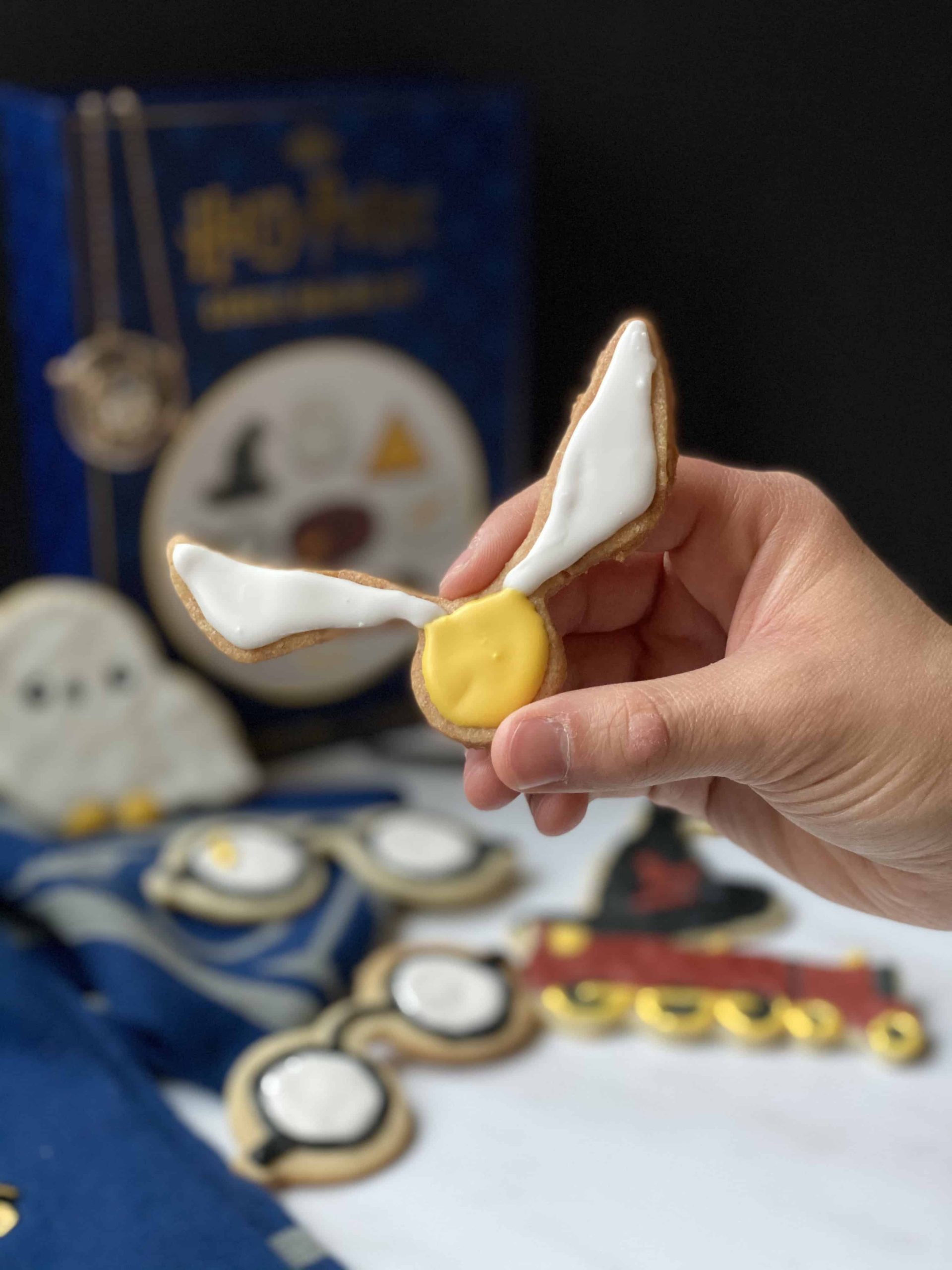 A hand holding a sugar cookie decorated like the golden snitch from Harry Potter.