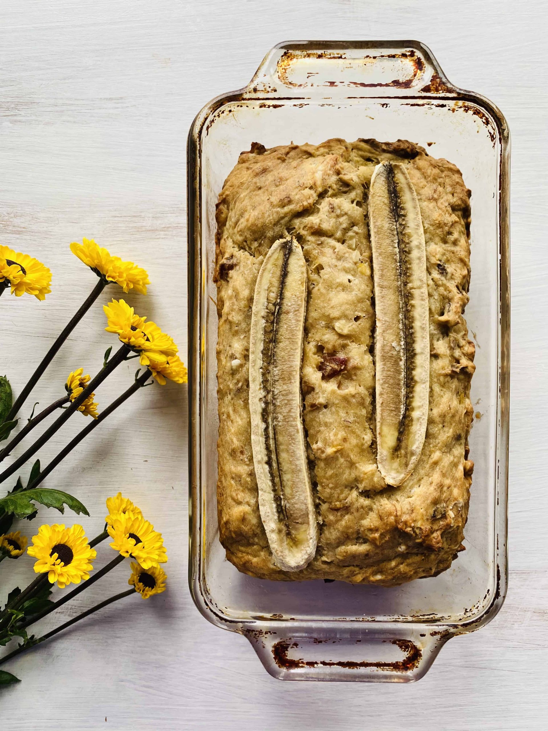 Walnut banana bread in a baking dish next to small yellow flowers.