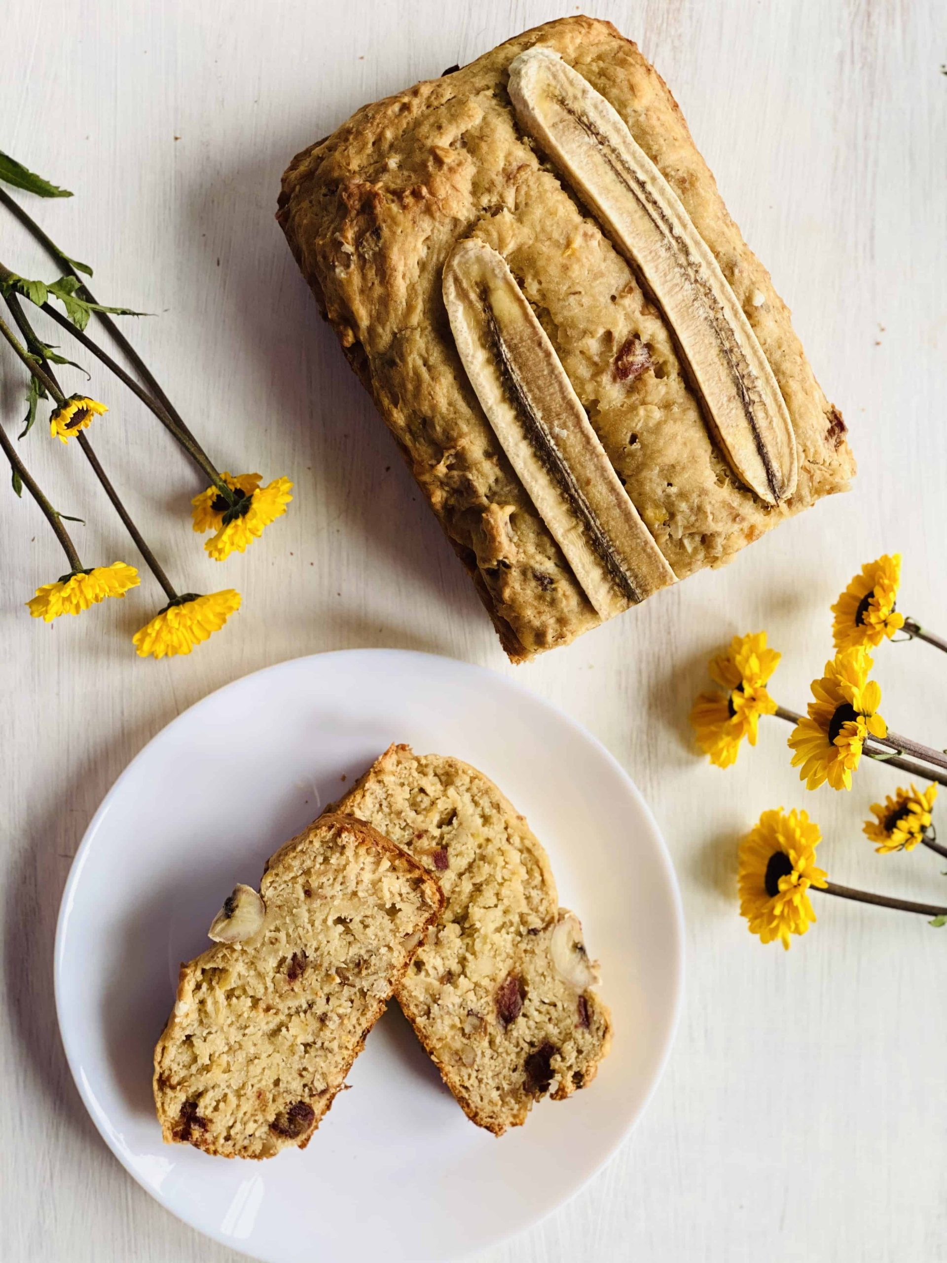A loaf of banana bread with two slices cut out and laid on a white plate.