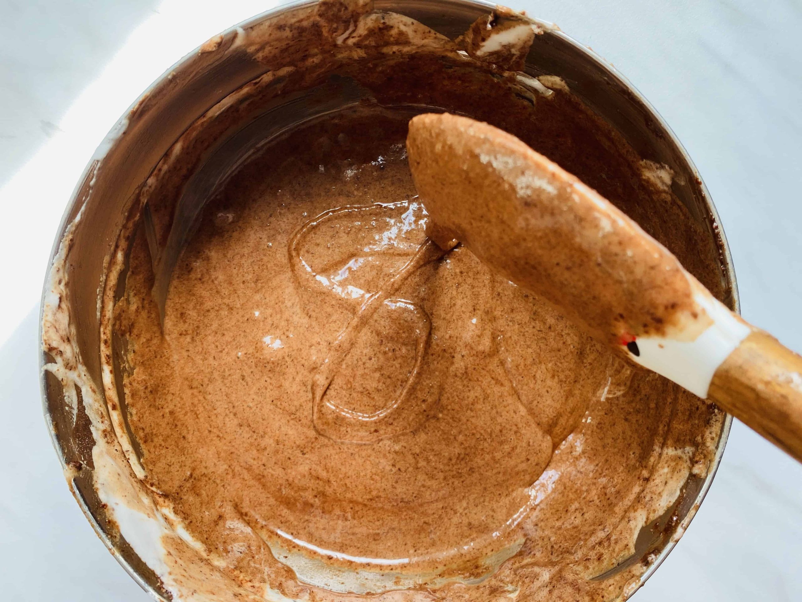 Chocolate macaron batter, being dripped off a spatula into a figure-8.