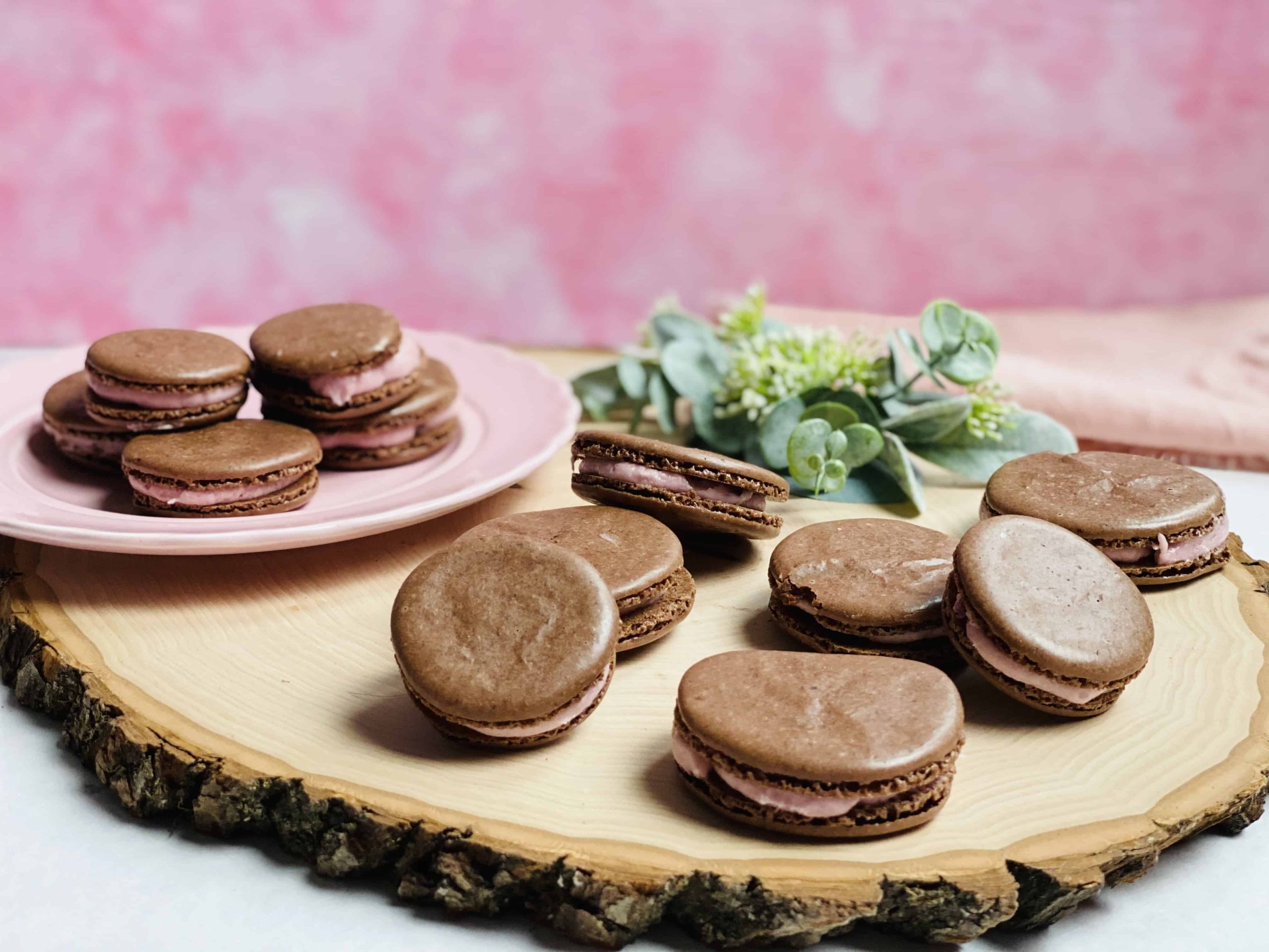 Chocolate strawberry macarons piled on a plate and a wooden board.