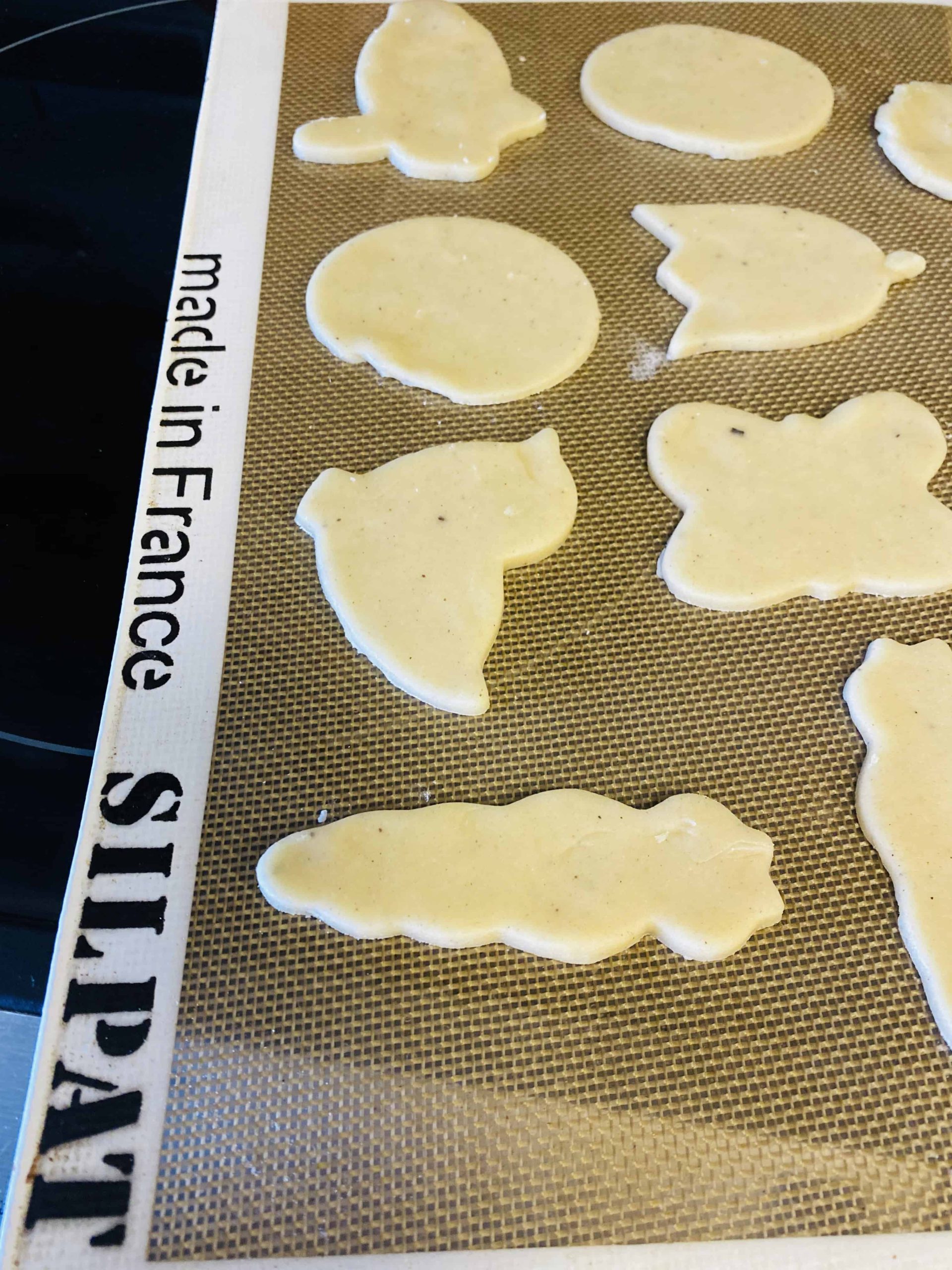 Unbaked cookies on a baking sheet shaped like carrots, chickens, and butterflies.