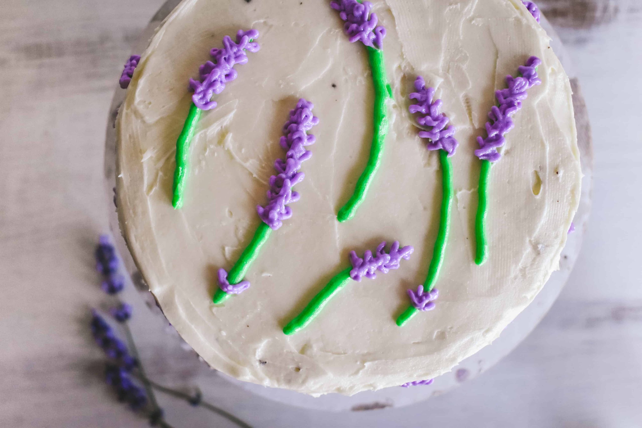 A round cake decorated with white frosting and purple and green buttercream flowers.