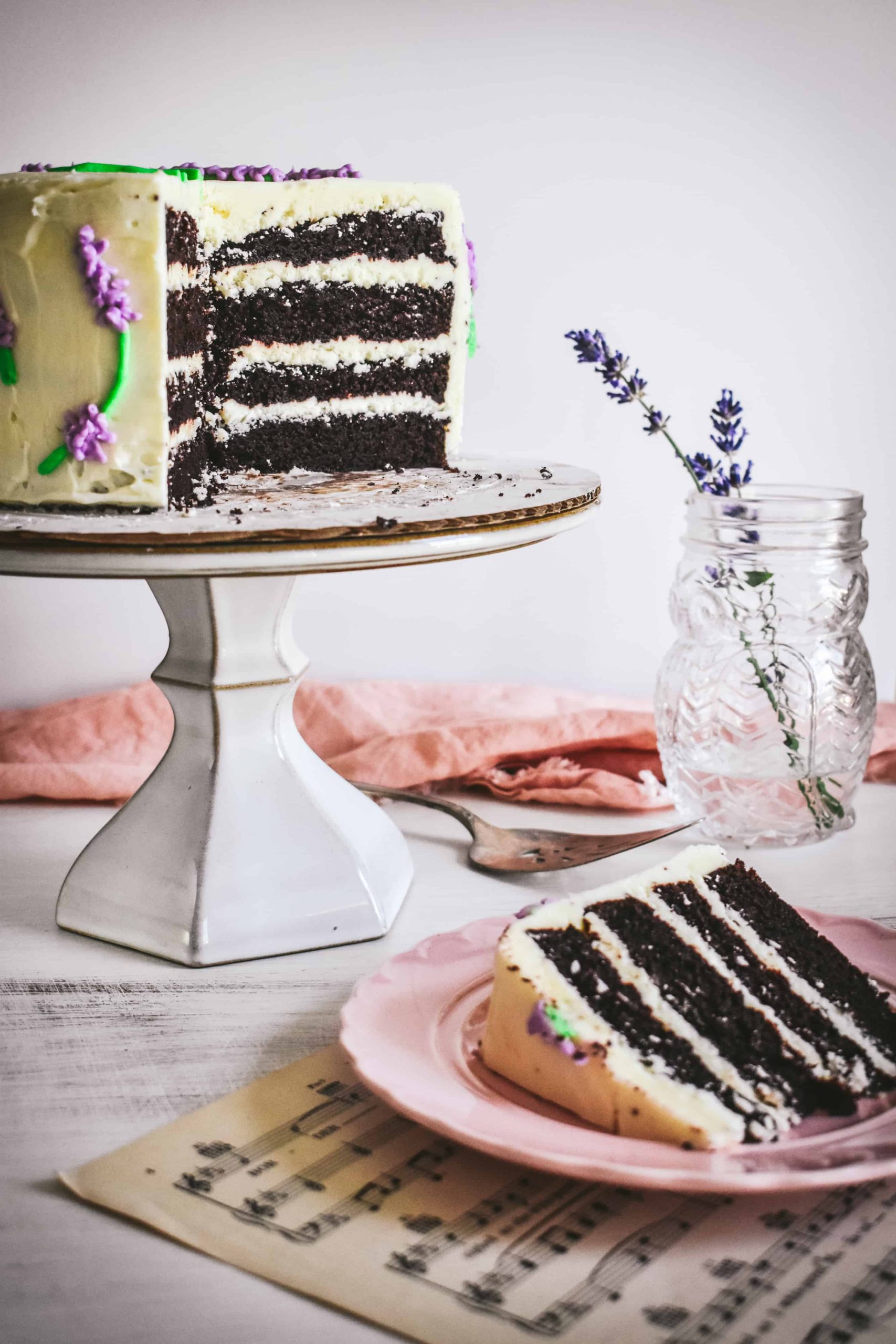 A four-layer cake with a few slices cut out of it next to fresh lavender in a glass jar.