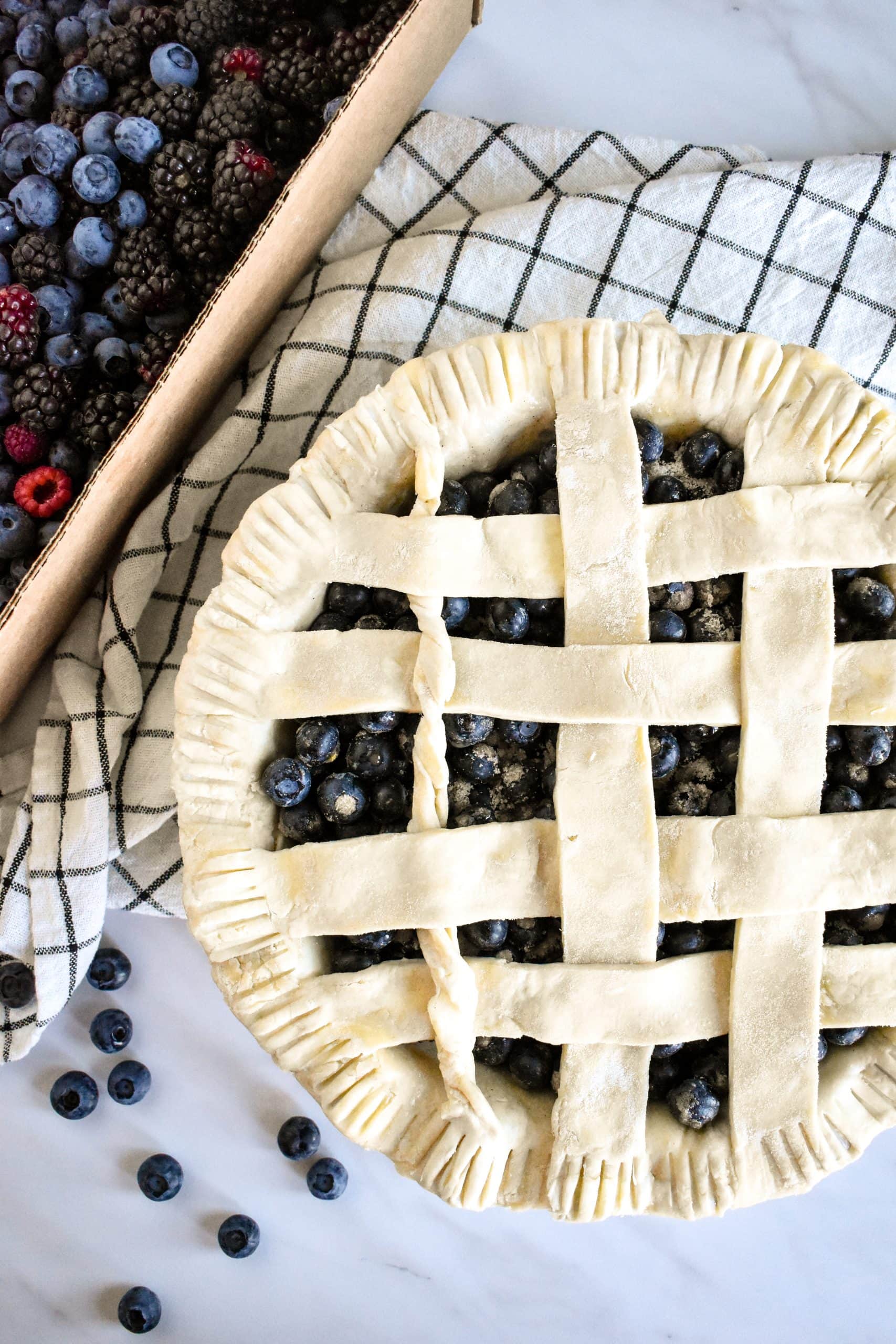 An unbaked pie crust shaped into a lattice design on top of fresh blueberries in a pie tin.