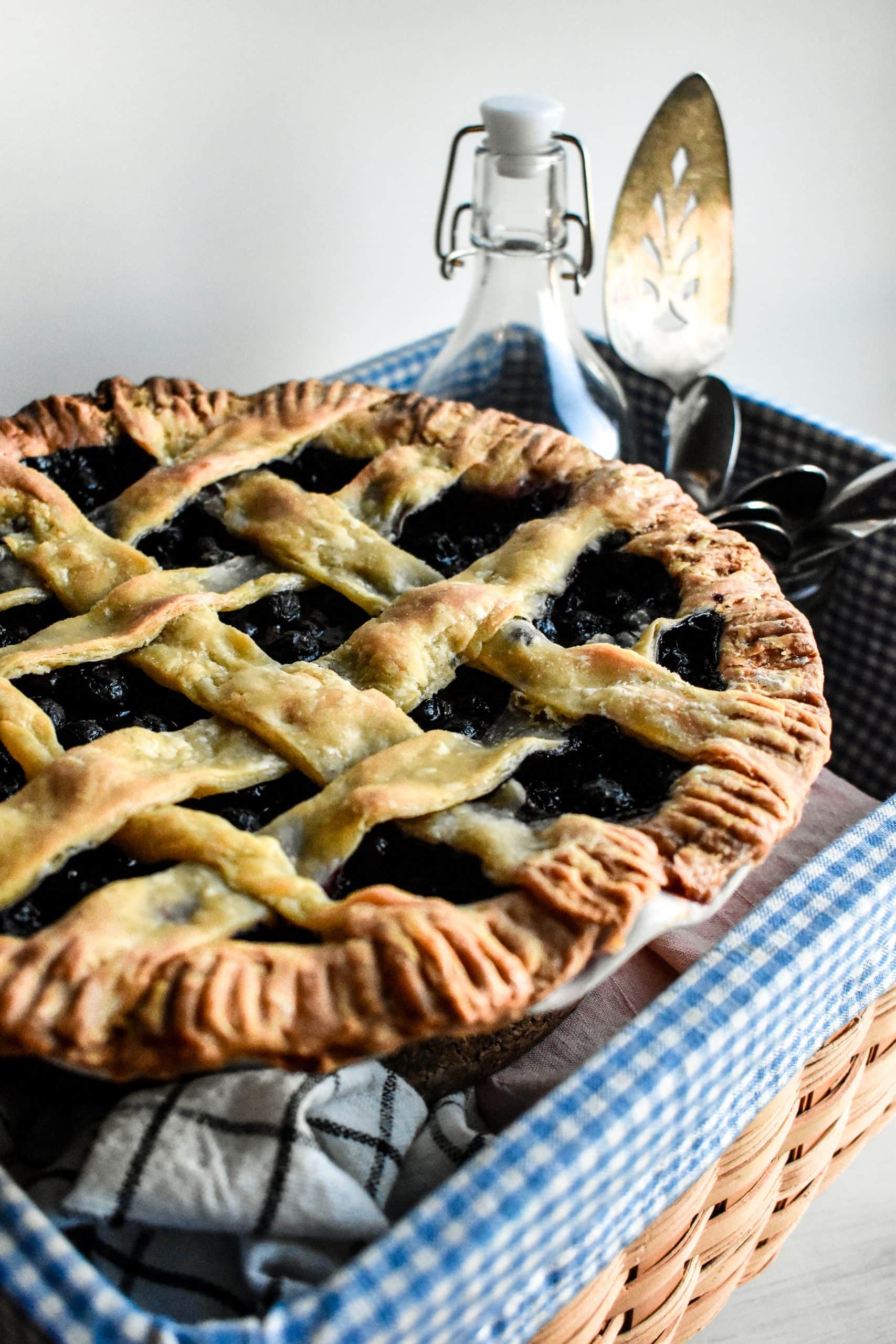 A baked Blueberry Pie in a basket with a glass bottle.