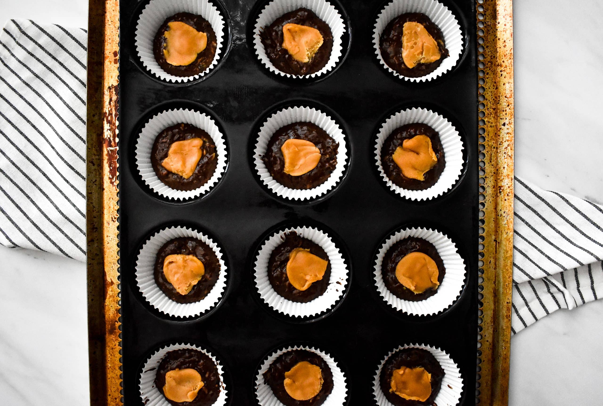 A dozen muffin cups filled with chocolate muffin batter and topped with caramel candy pieces.