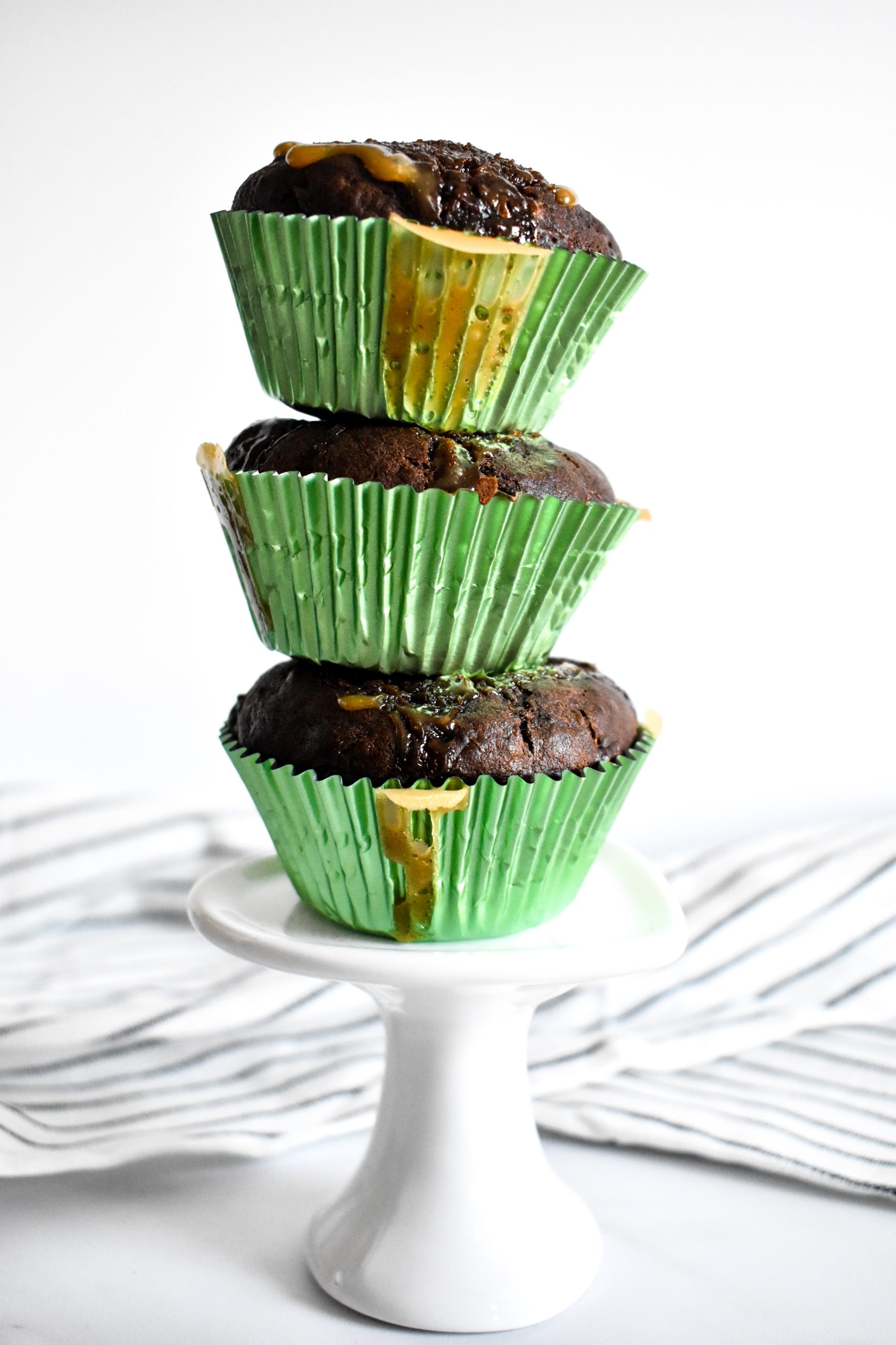 Three chocolate muffins stacked on top of each other in green muffin liners.
