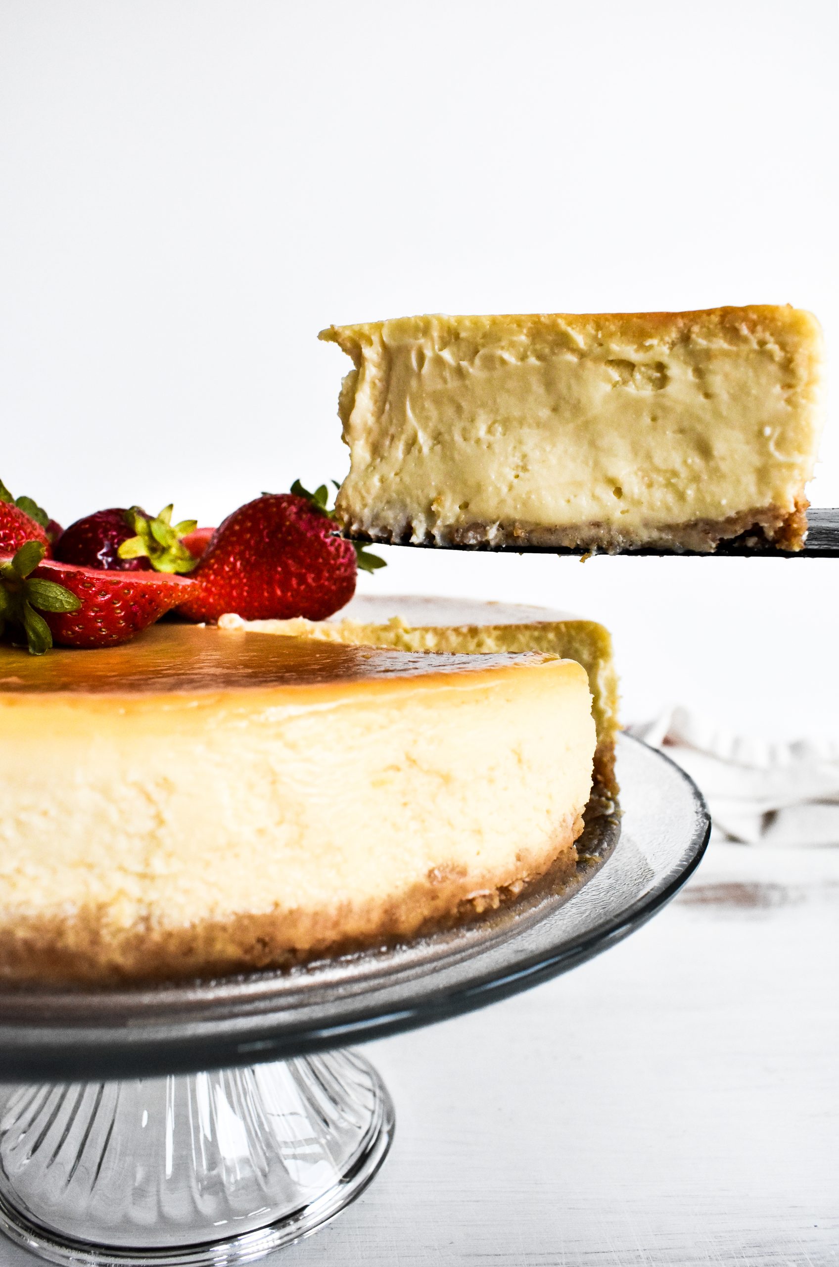 A knife lifting up a thick slice of cheesecake from the rest of the cake.