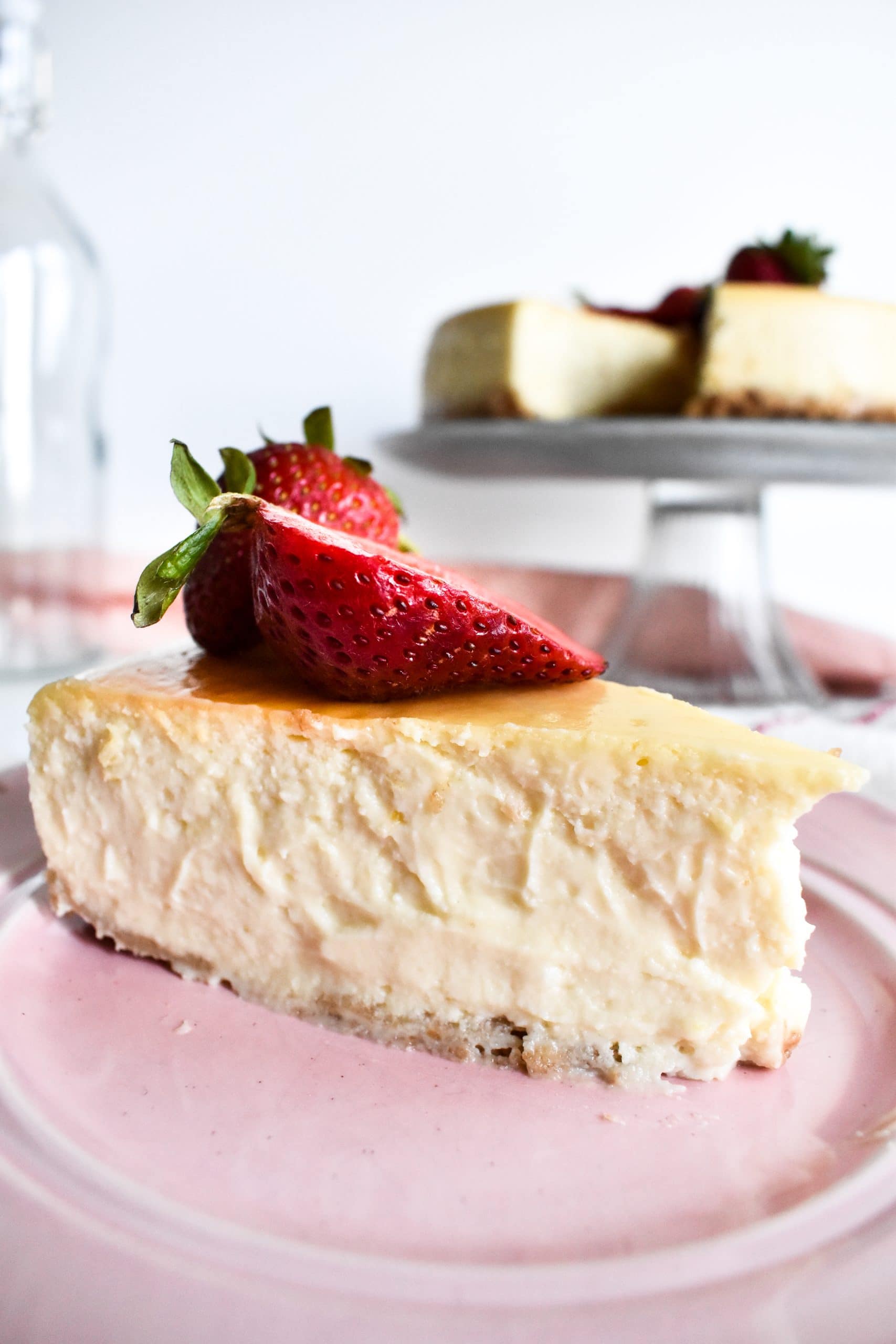 A creamy and thick slice of cheesecake on a pink plate with fresh strawberries on top.