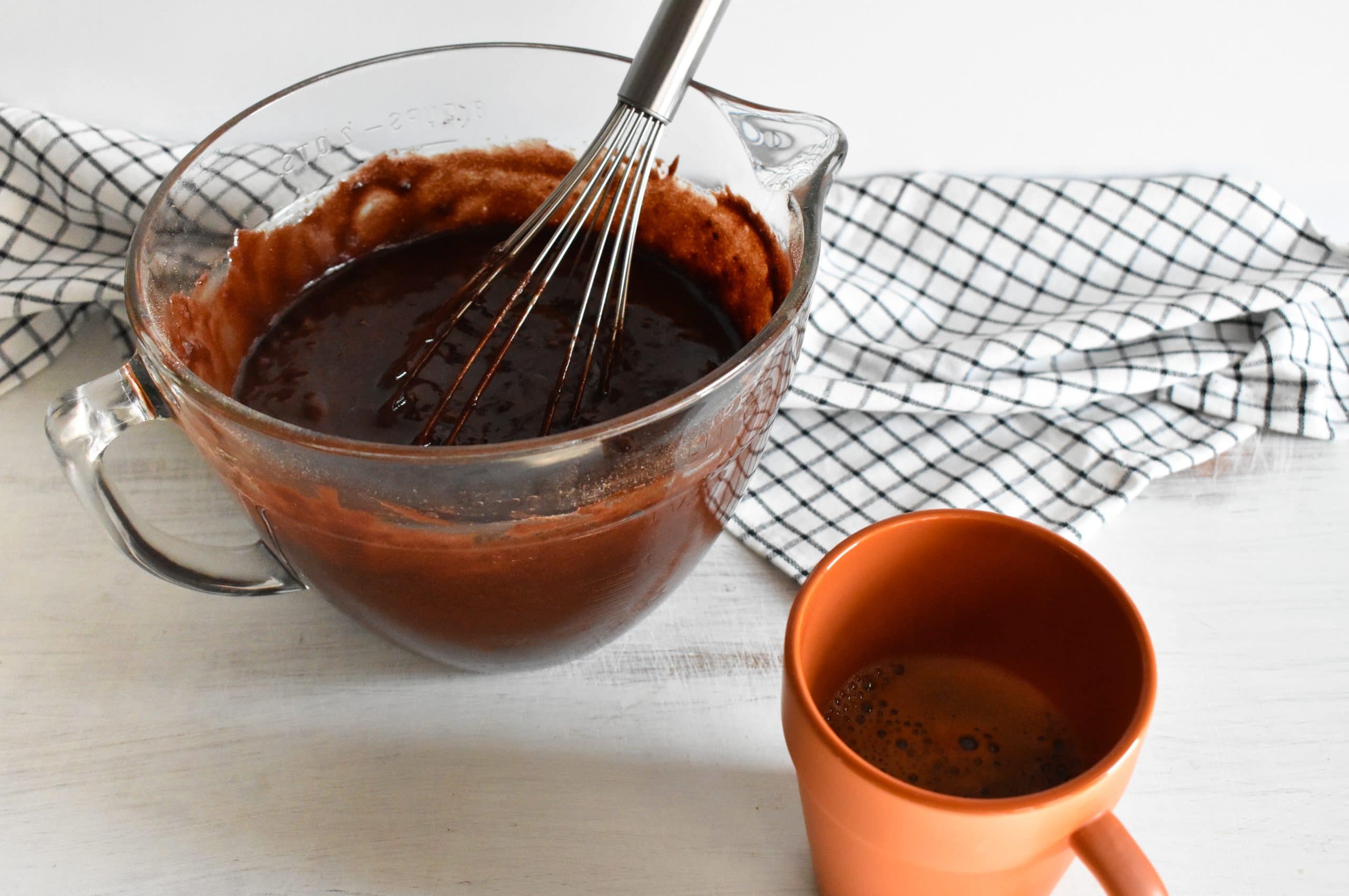 Chocolate cake batter in a bowl next to a mug of coffee.