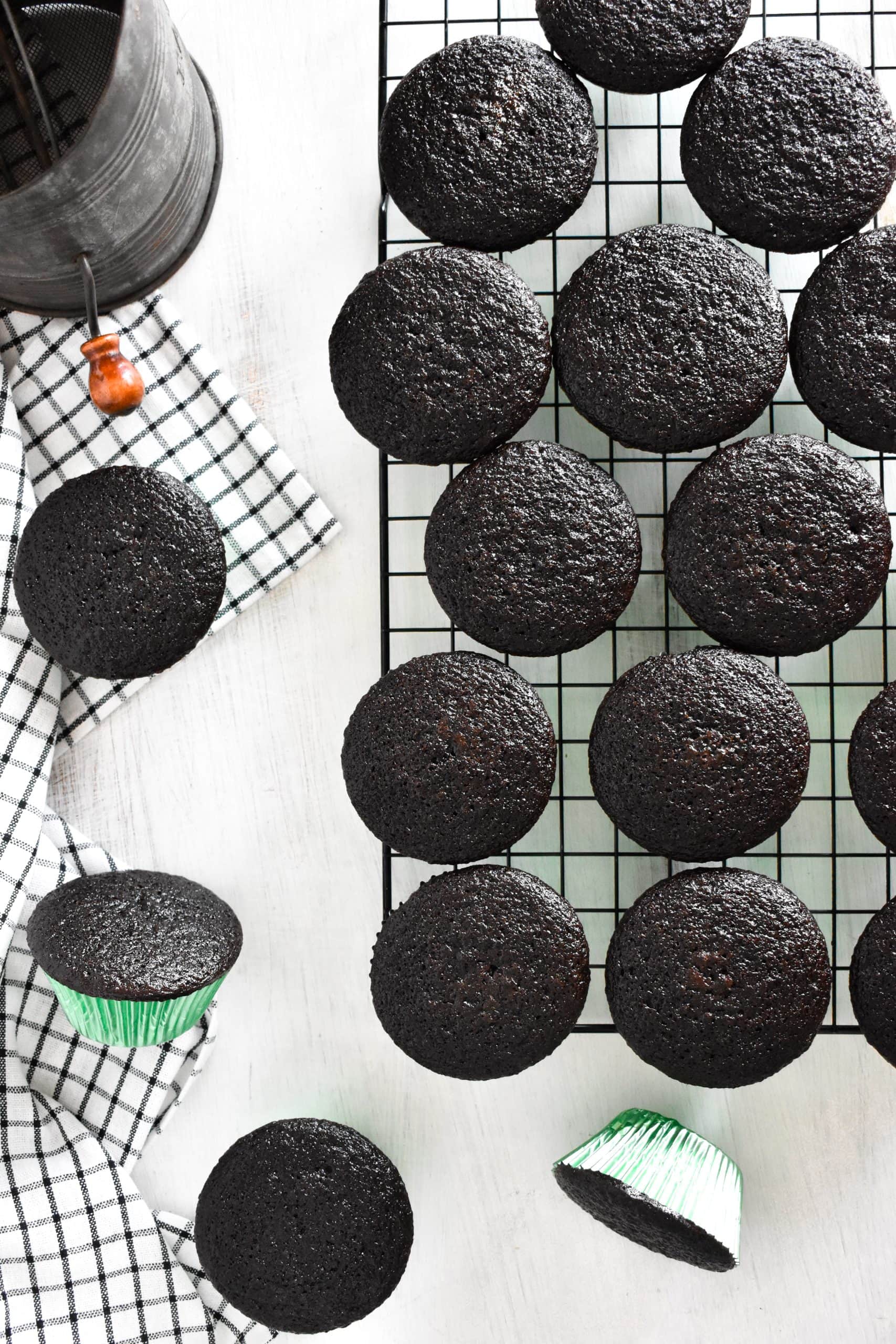 Black chocolate cupcakes in green cupcake cups on a cooling rack.