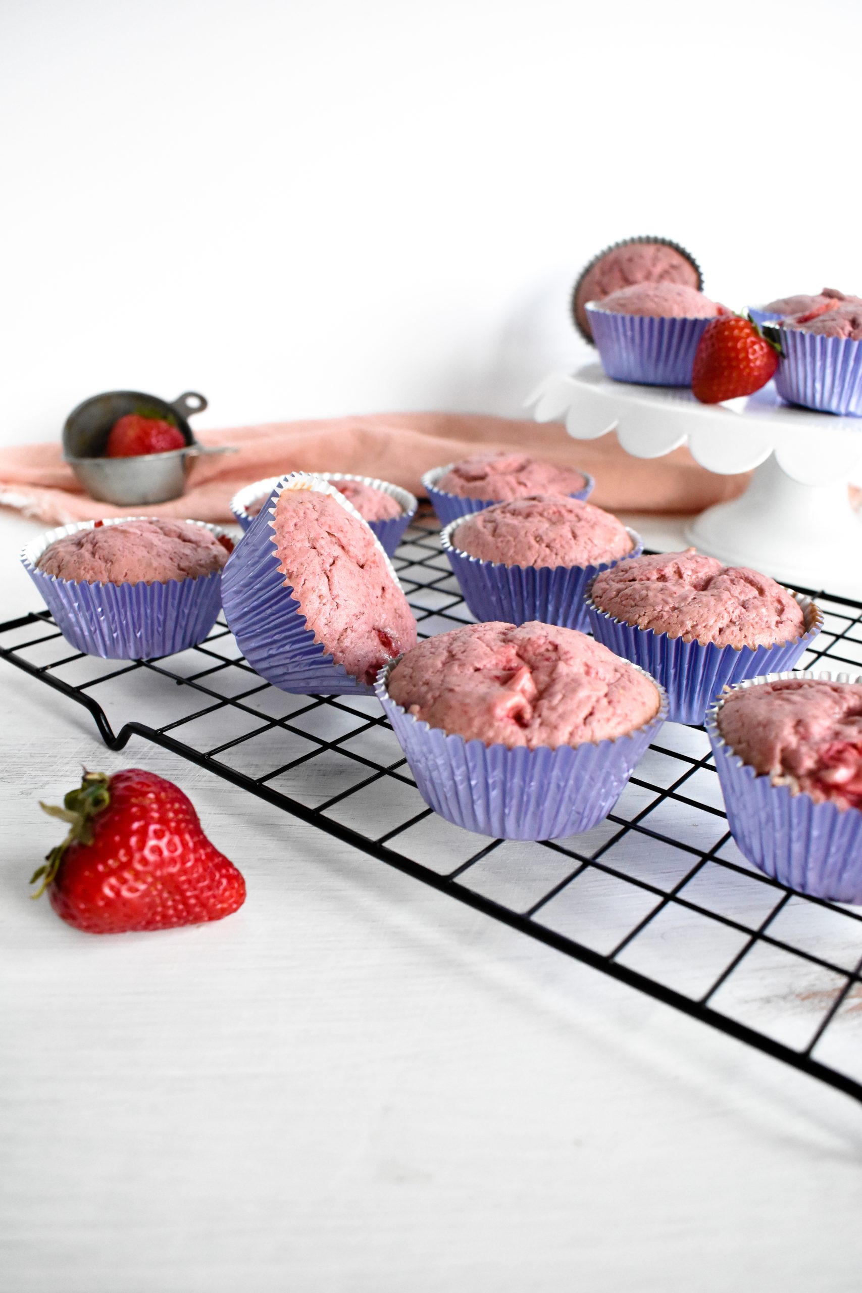 Pink strawberry cupcakes in purple cupcake cups on a cooling rack.