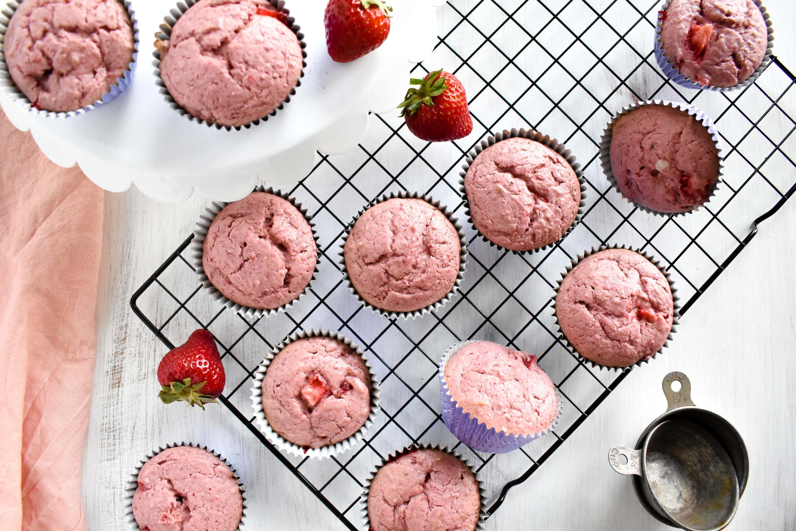 Overhead view of a dozen pink strawberry cupcakes on a black cooling rack.