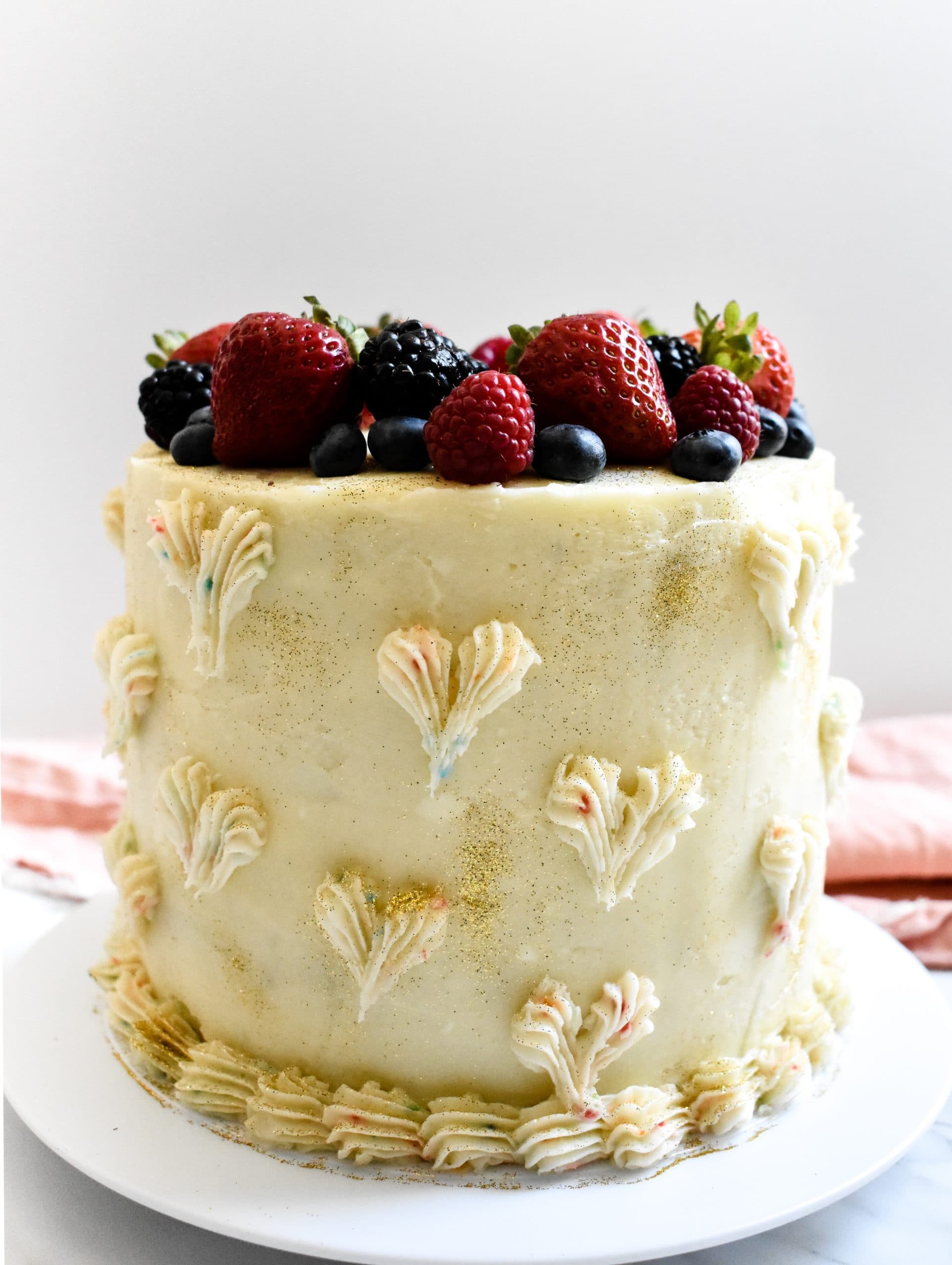 A white wedding cake topped with fresh berries on a cake platter. 
