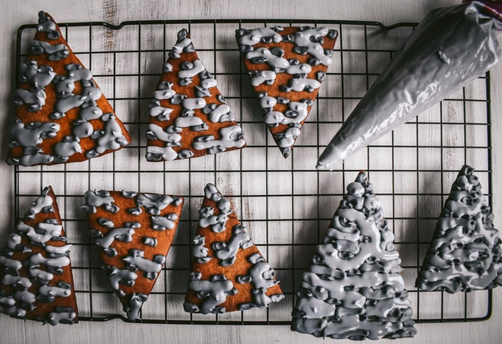piping bag full of gray royal icing to pipe stone-looking patterns on gingerbread house roof pieces