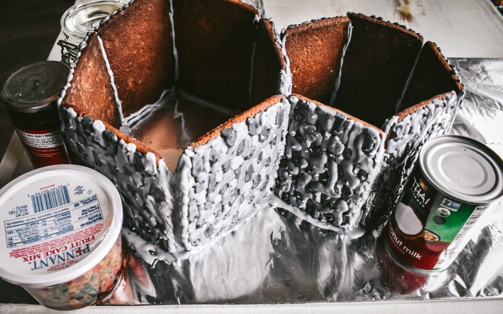 homemade gingerbread house being constructed and propped up with jars and cans while it dries