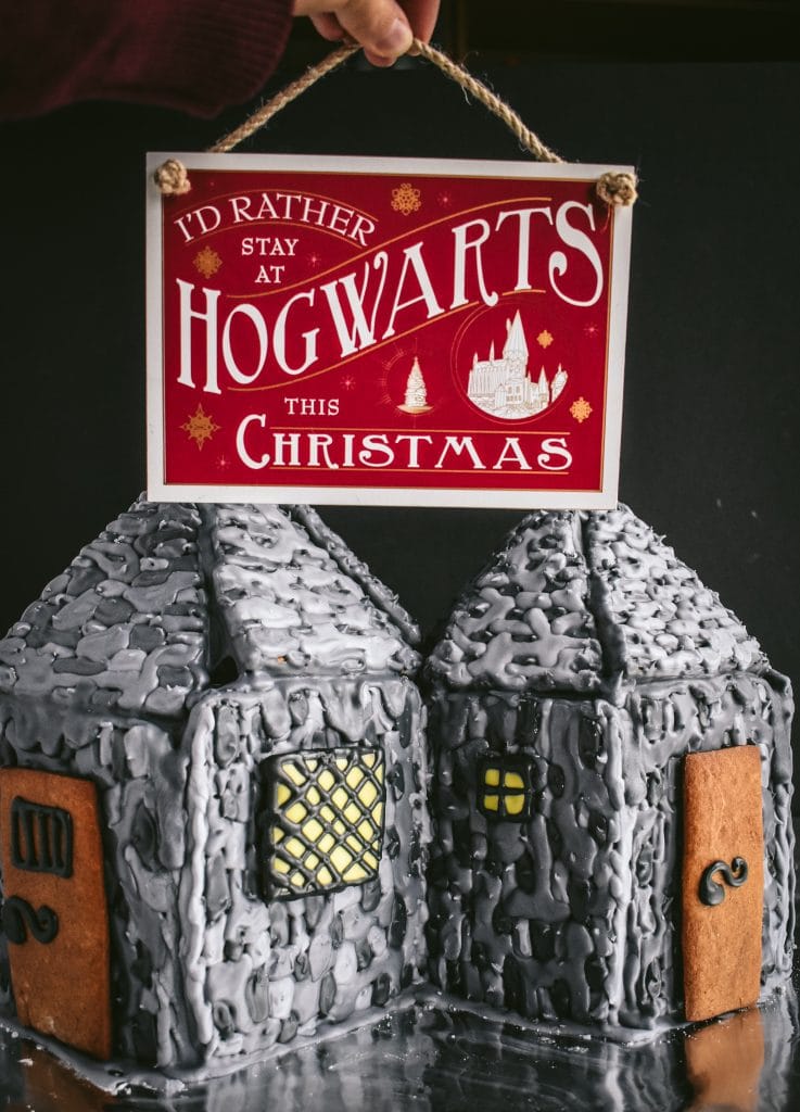 hand holding a Hogwarts Christmas sign over Hagrid's Hut Gingerbread House