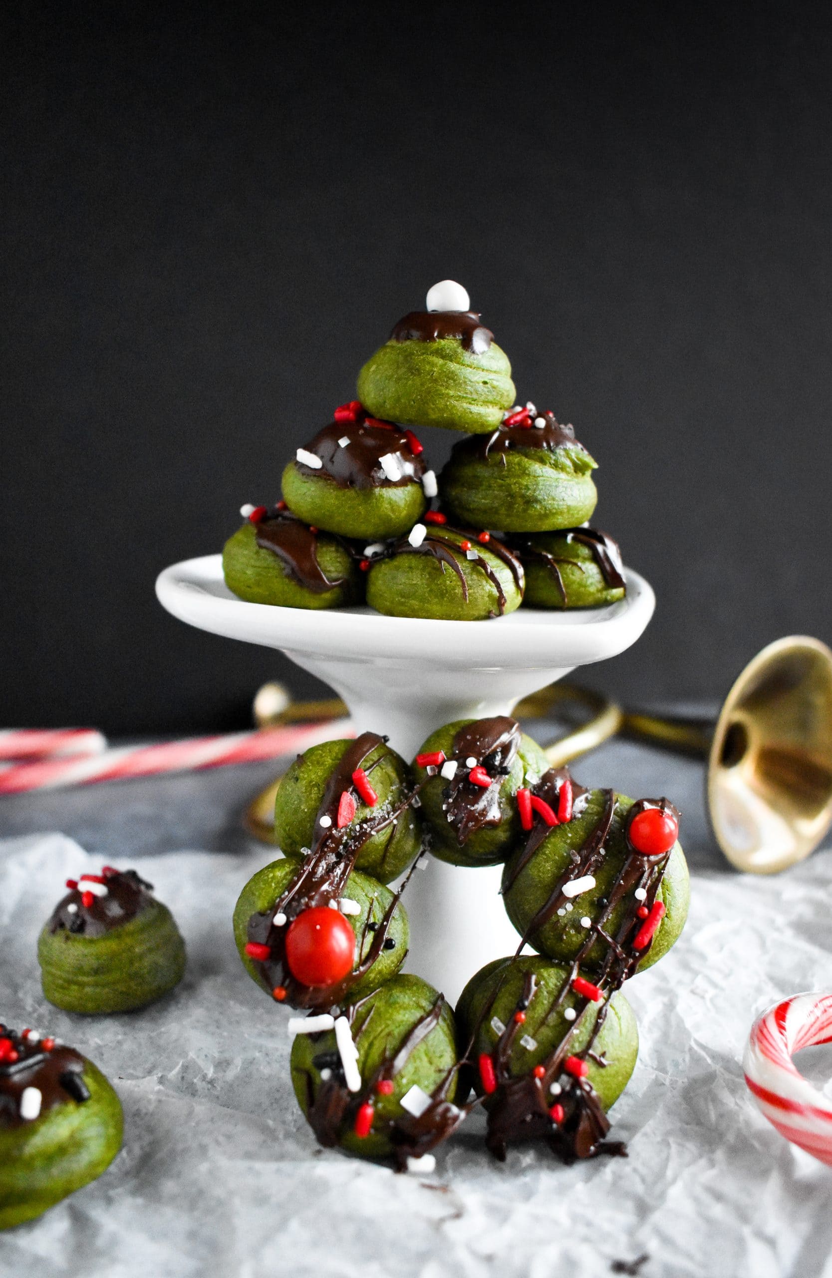 A stack of small green donut bubbles topped with melted chocolate and sprinkles.