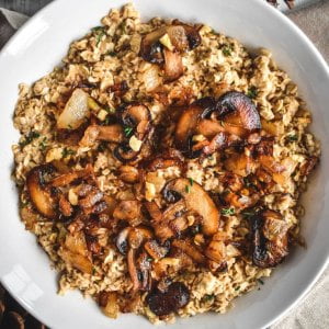 A bowl filled with oatmeal, caramelized mushrooms, finely chopped herbs, and chopped onions.