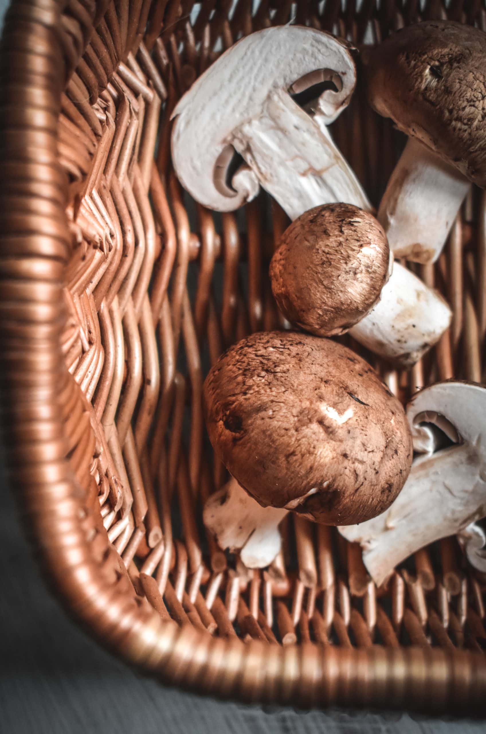 A wicker basket filled with whole and sliced mushrooms.