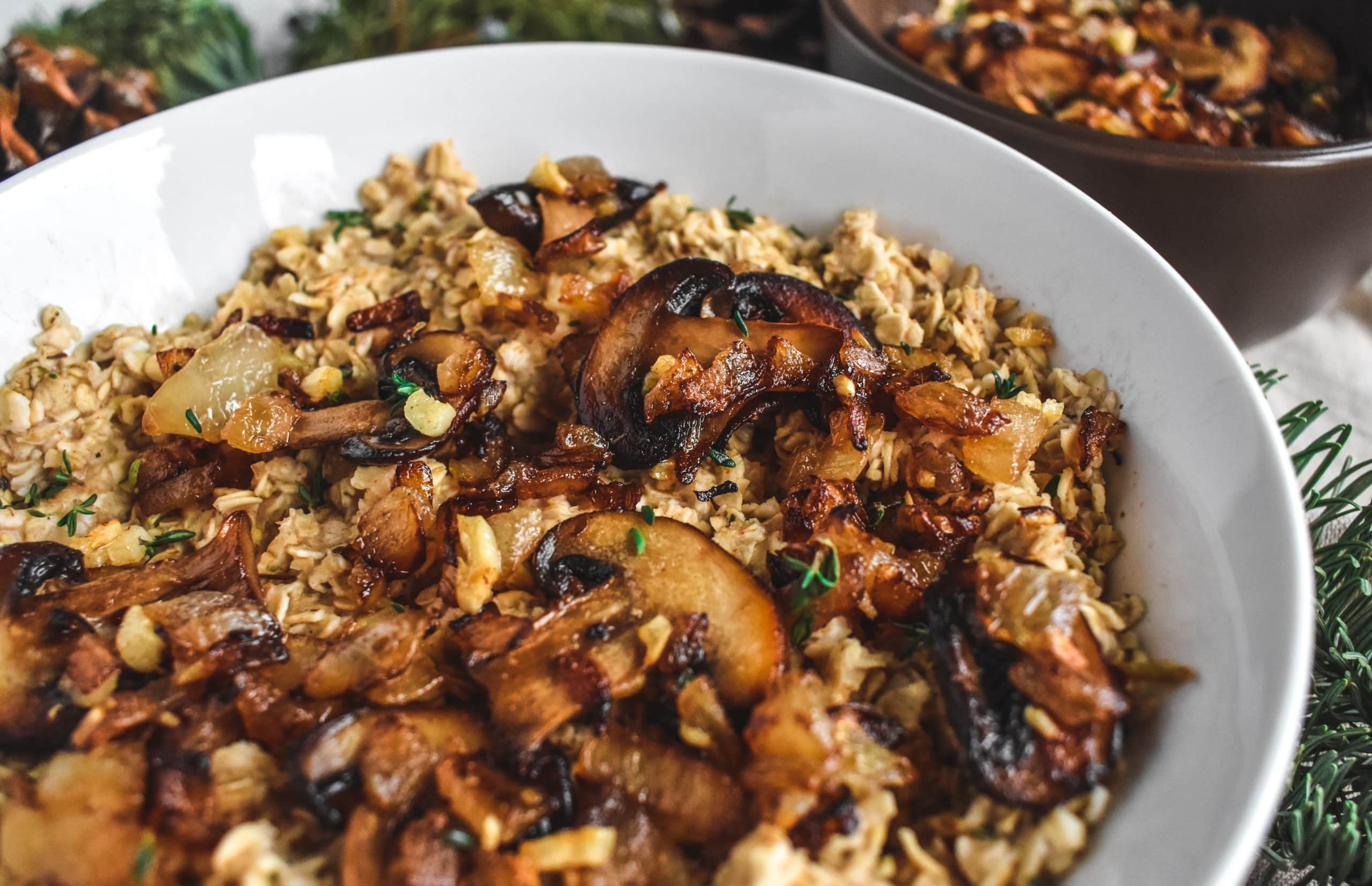 A white bowl filled with cooked oatmeal, mushrooms, and onions topped with chopped thyme.