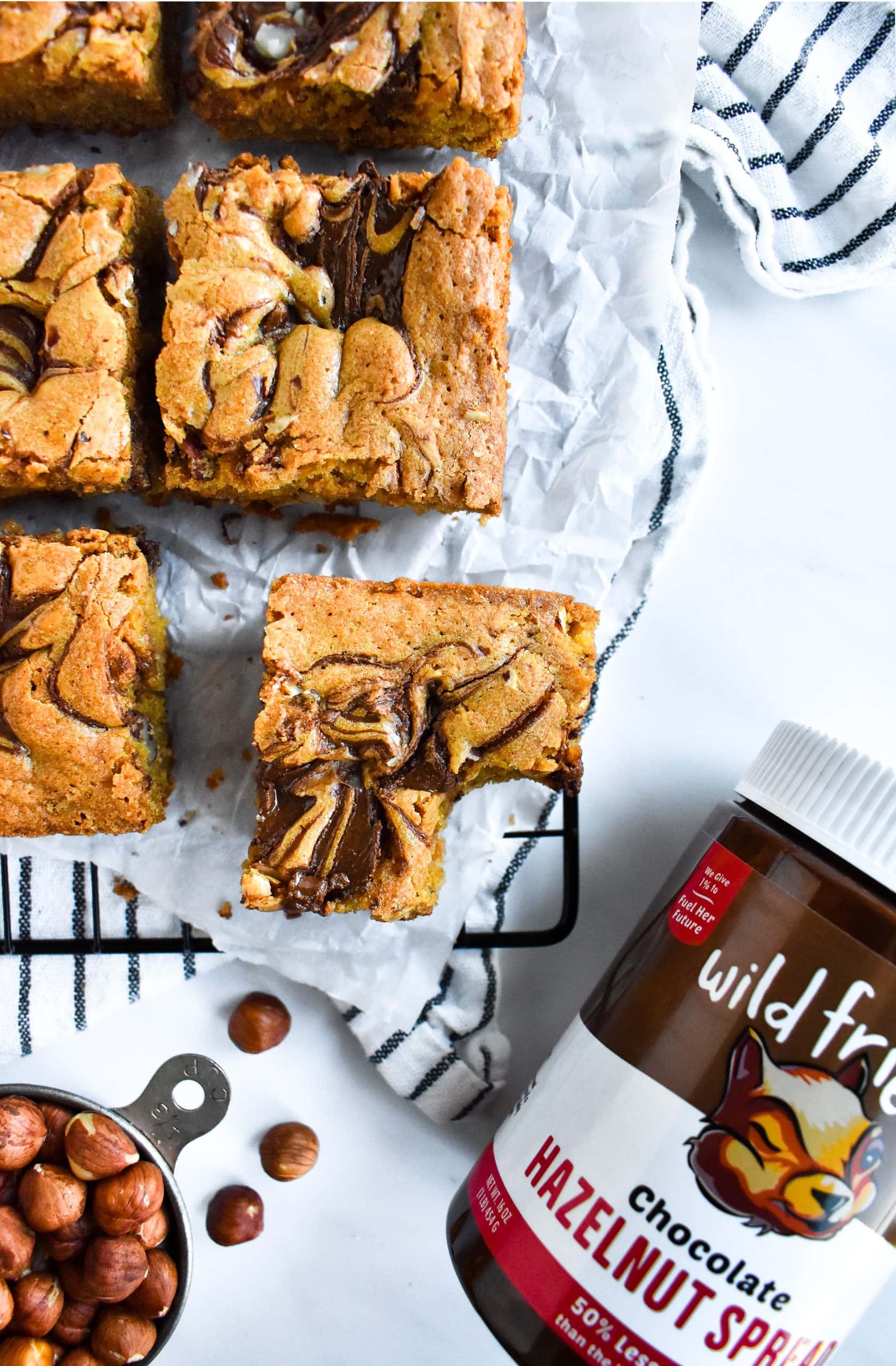 An overhead view of a blondie with a bite taken out, next to a jar of chocolate hazelnut spread.