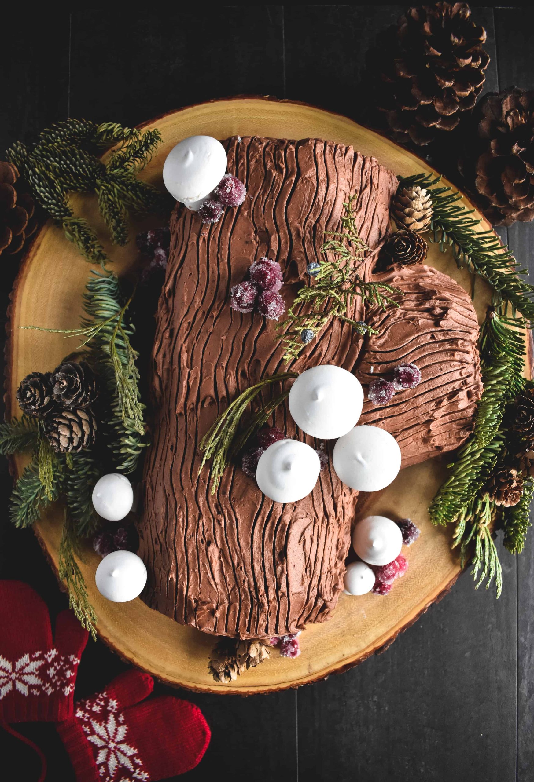 An overhead view of a yule log cake decorated with meringue mushrooms and candied cranberries. 