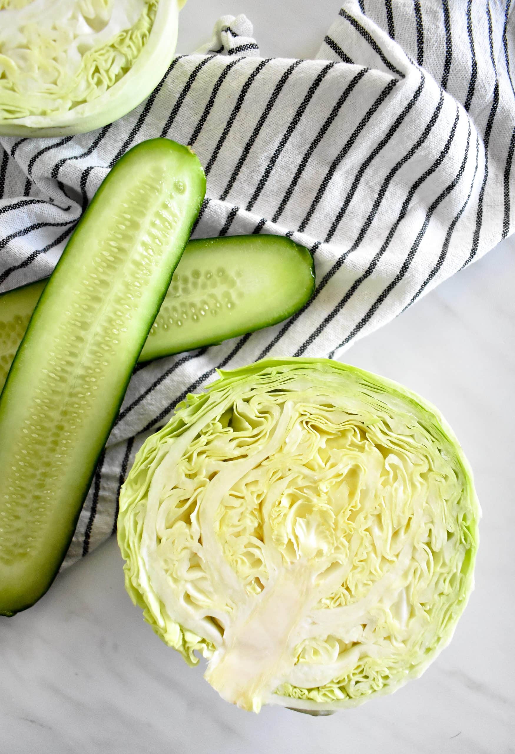 Half a head of cabbage and a sliced cucumber on a black and white kitchen towel.