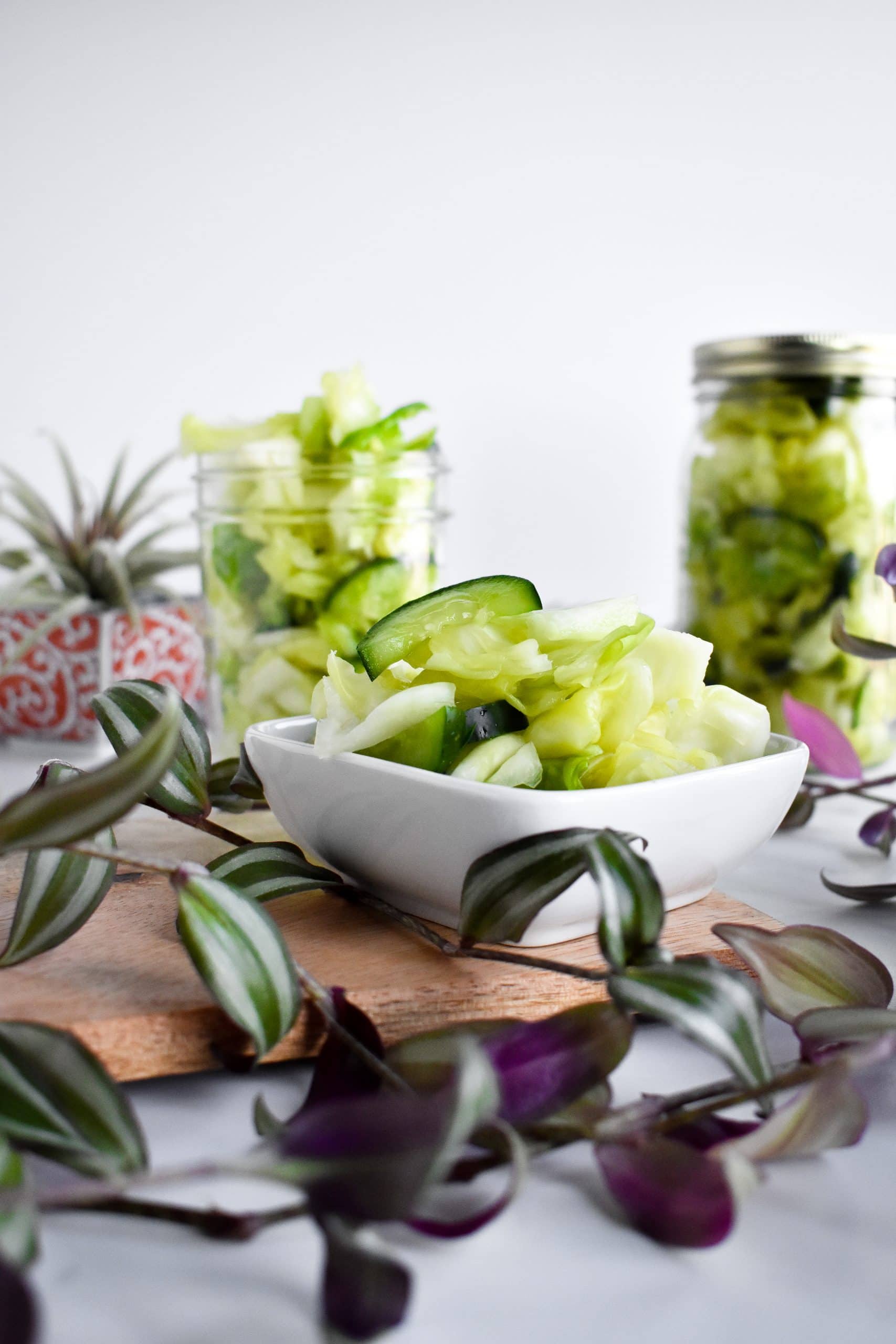 Two glass mason jars and a white plate filled with mild green kimchi.