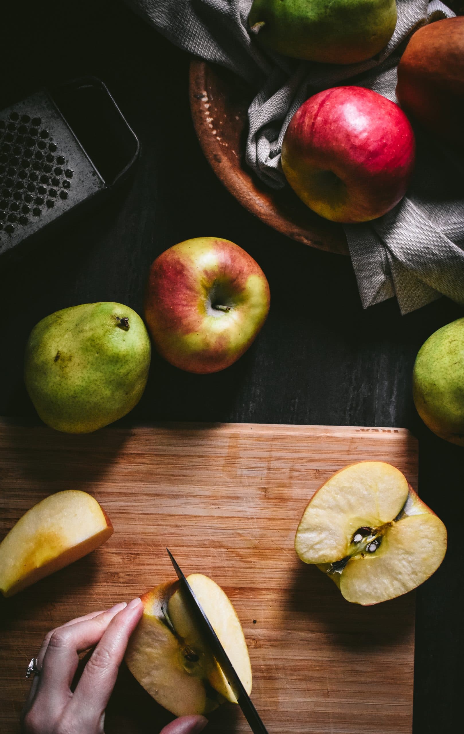 A hand chopping an apple on a bamboo cutting board.