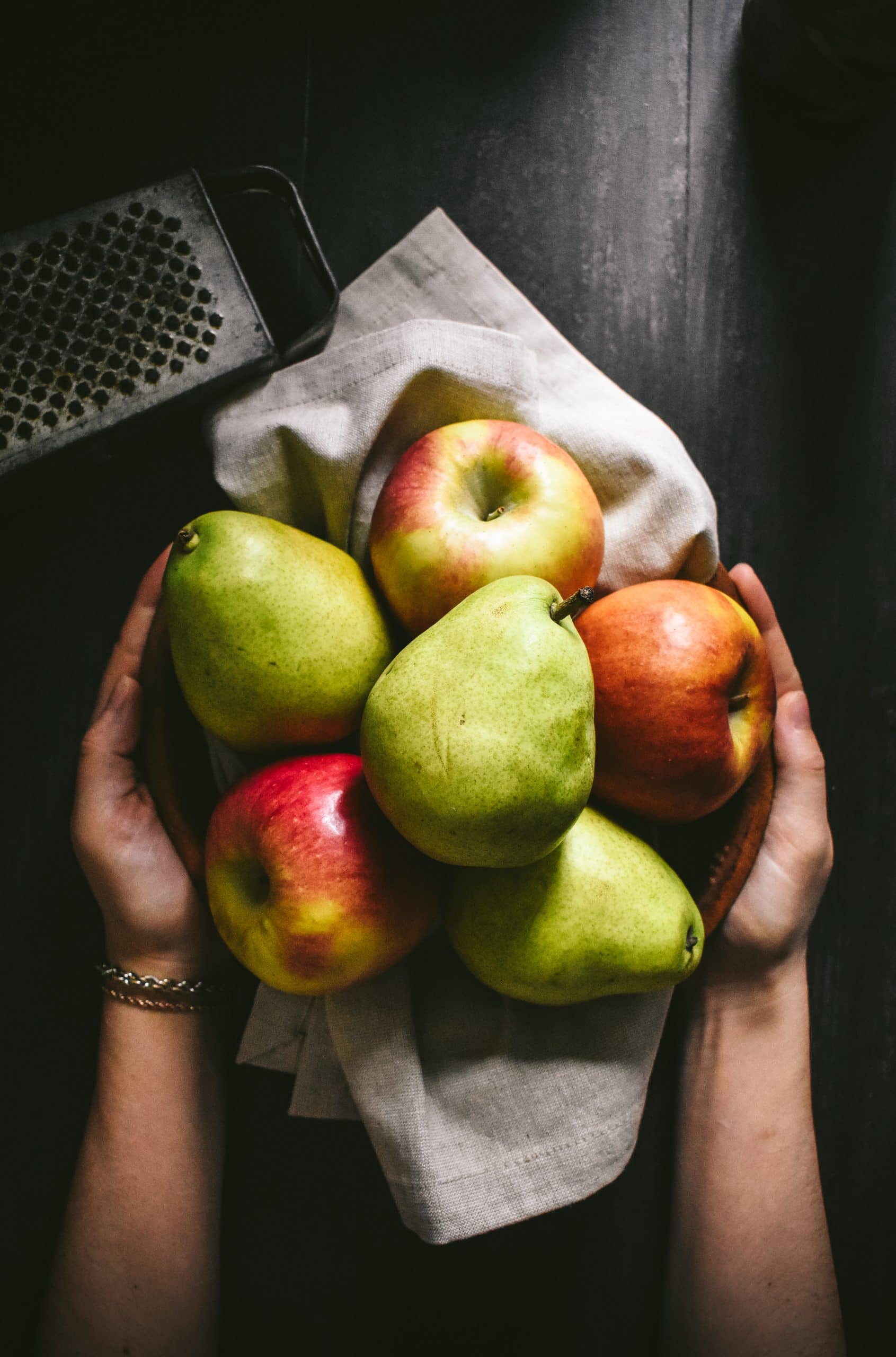 A hand holding a bowl filled with fresh apples and pears.