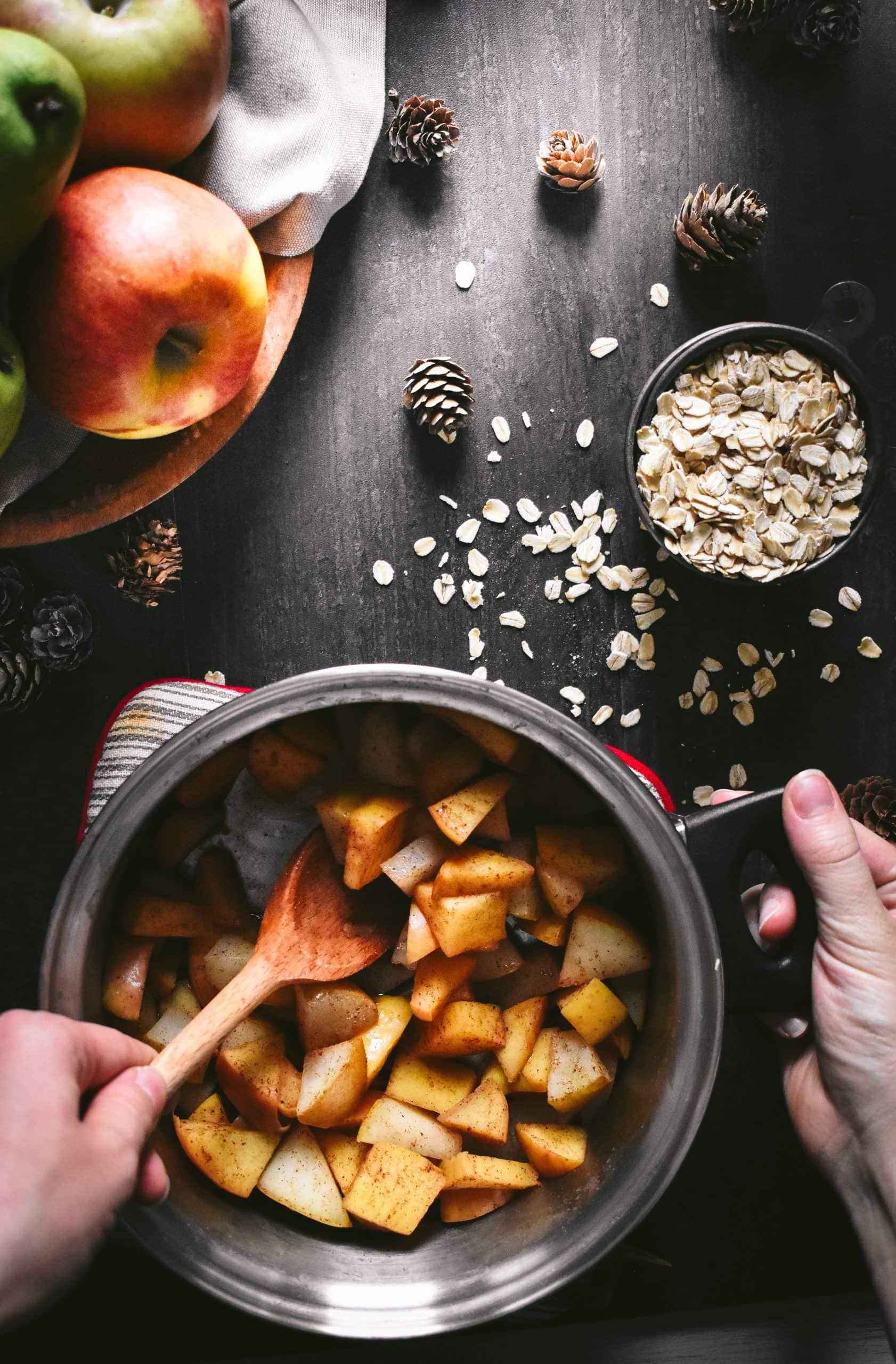 A hand stirring a saucepan filled with chopped apples, pears, and ground spices.