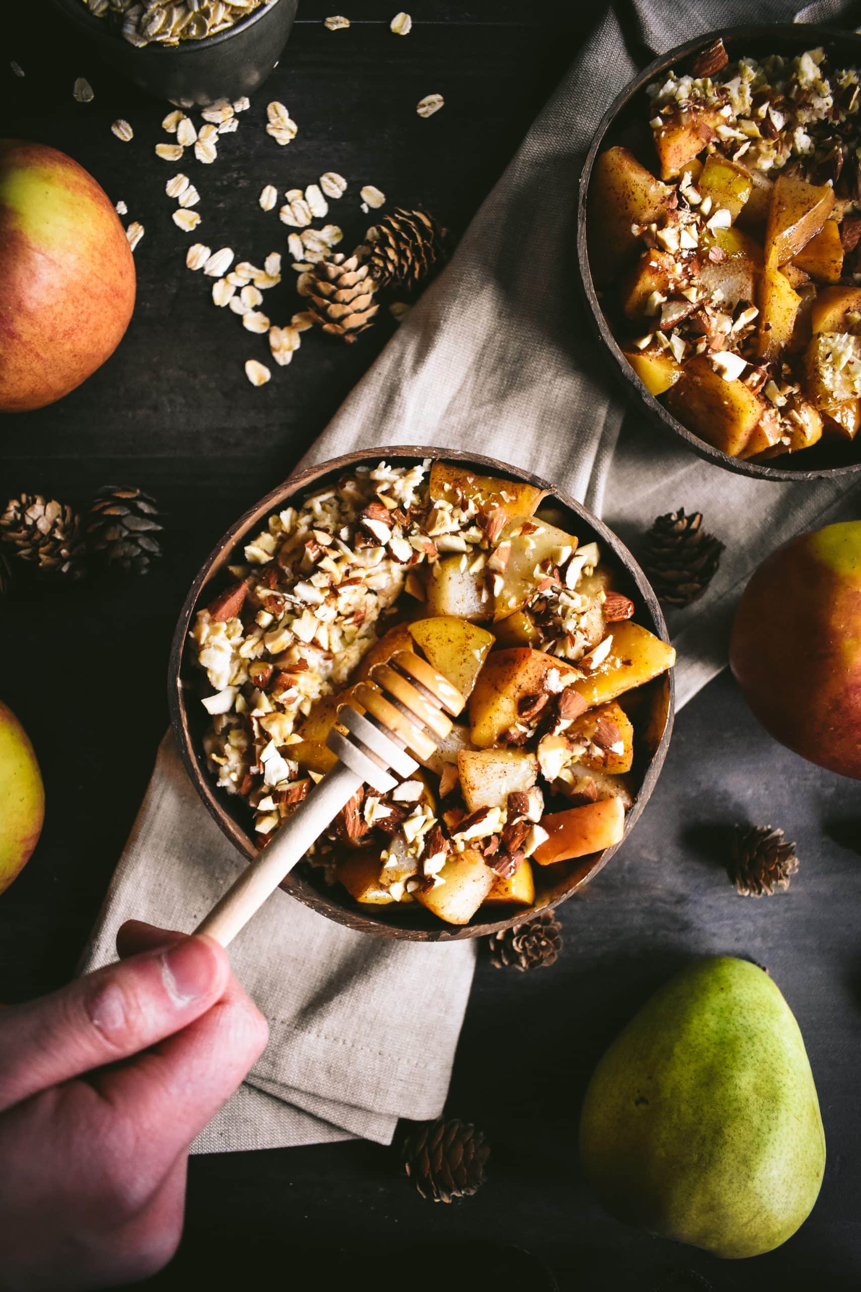 A hand drizzling honey from a honey stick onto oatmeal in a small bowl.