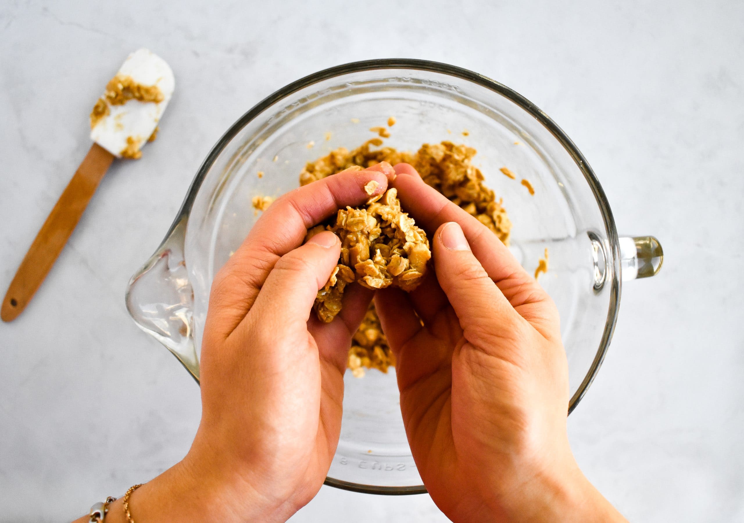 Two hands rolling a peanut butter and oat mixture into a small ball over a mixing bowl.