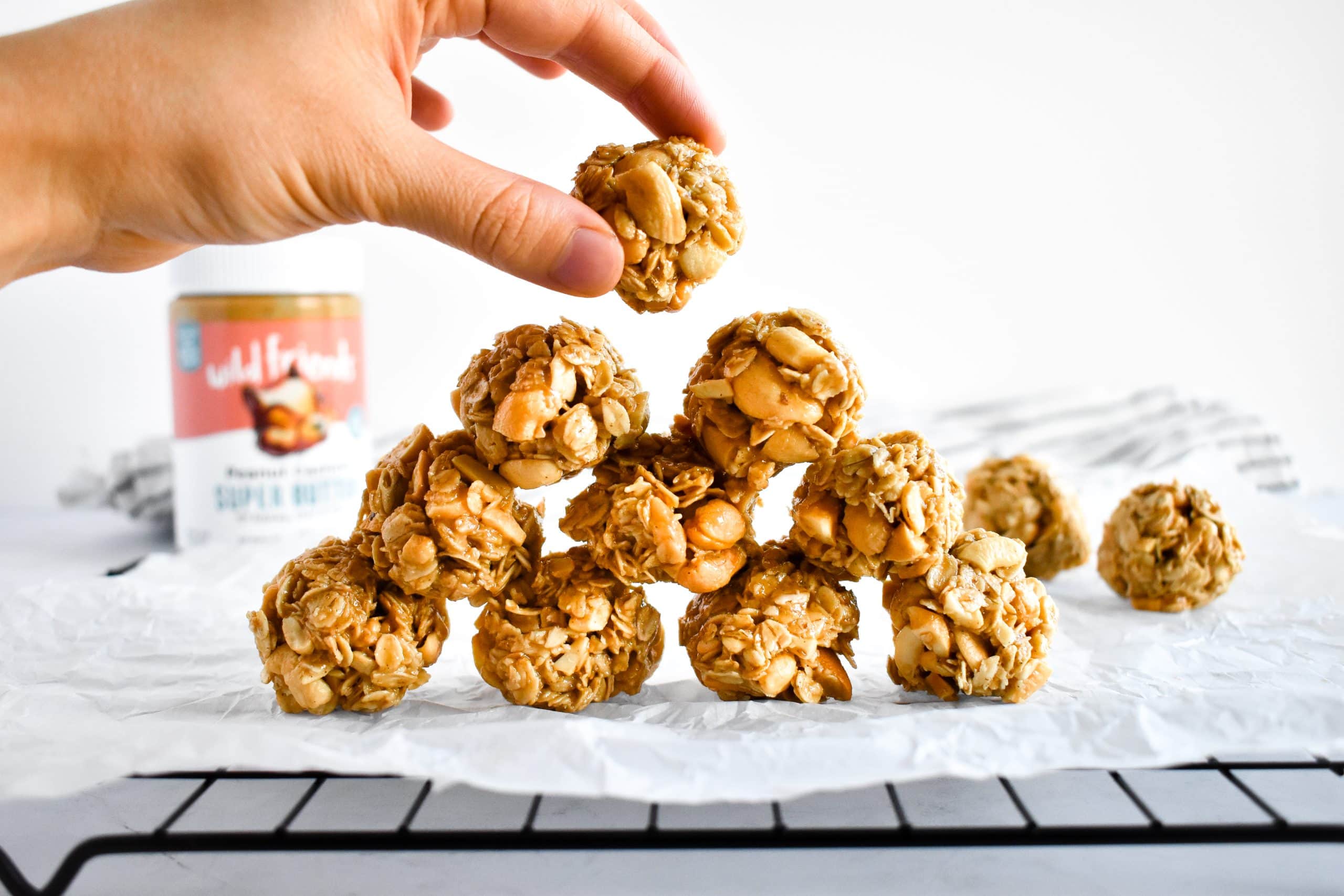 A hand picking up a peanut oatmeal ball from a stack on parchment paper.