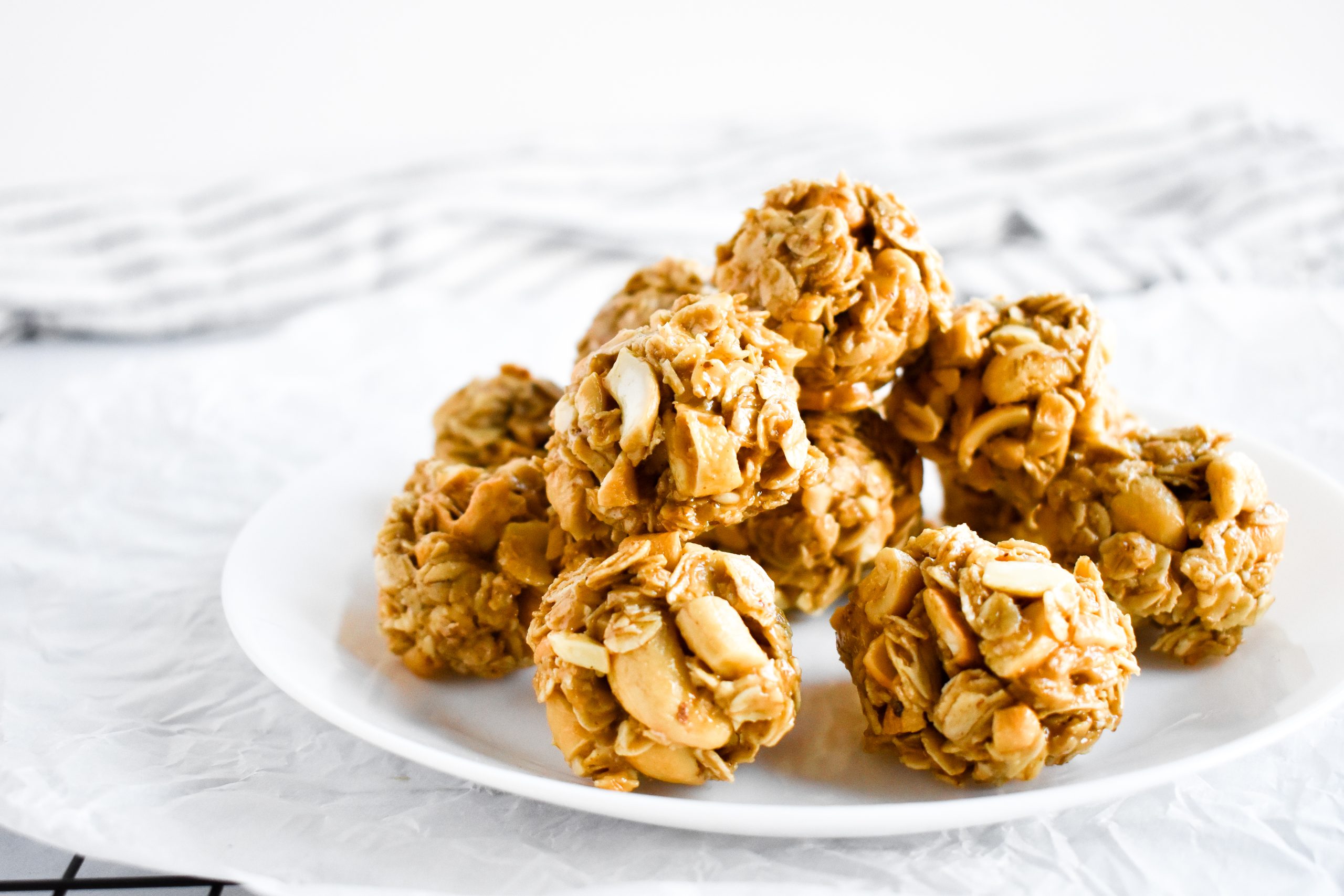 A white plate topped with a dozen energy balls made with oats and chopped peanuts. 