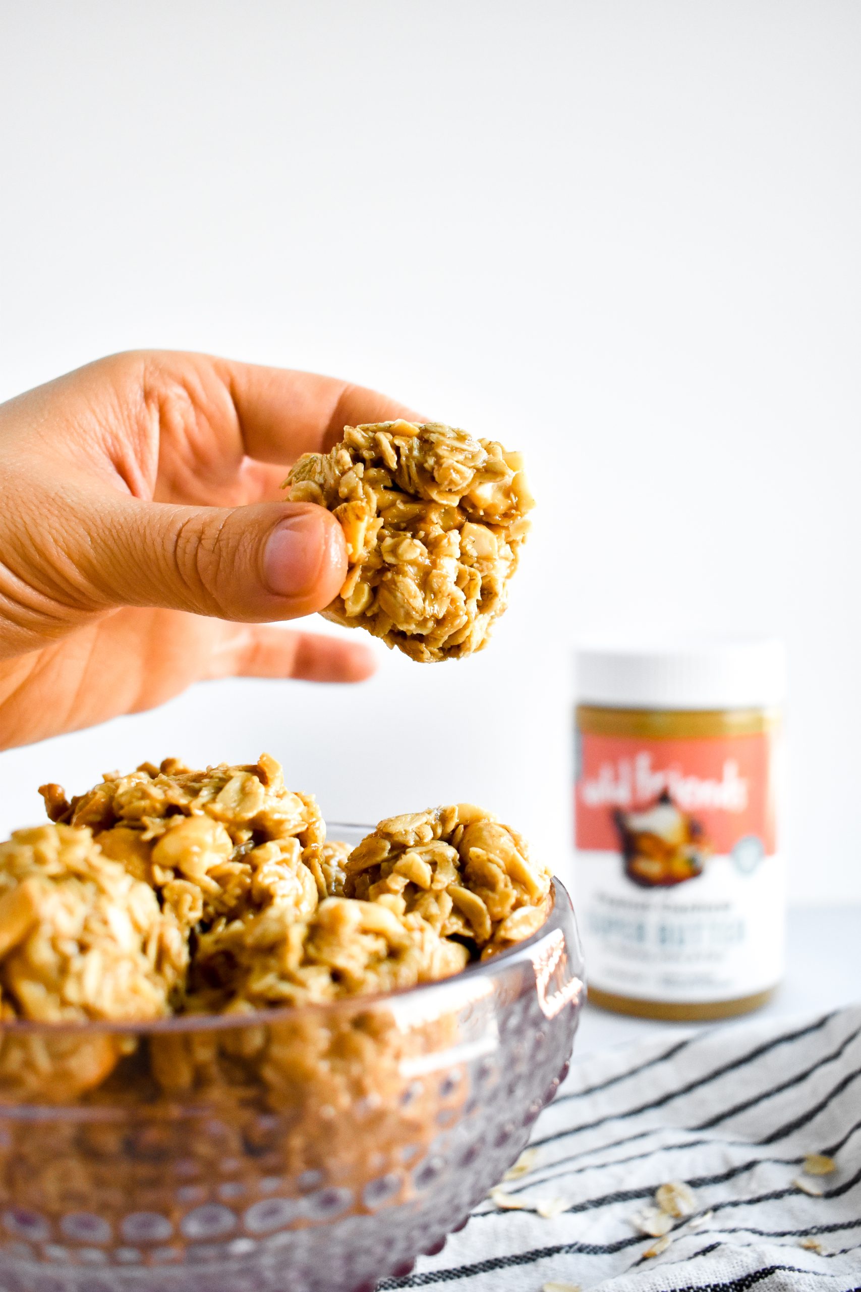 A hand holding a ball of oats, peanuts, and peanut butter over a bowl of more energy bites.