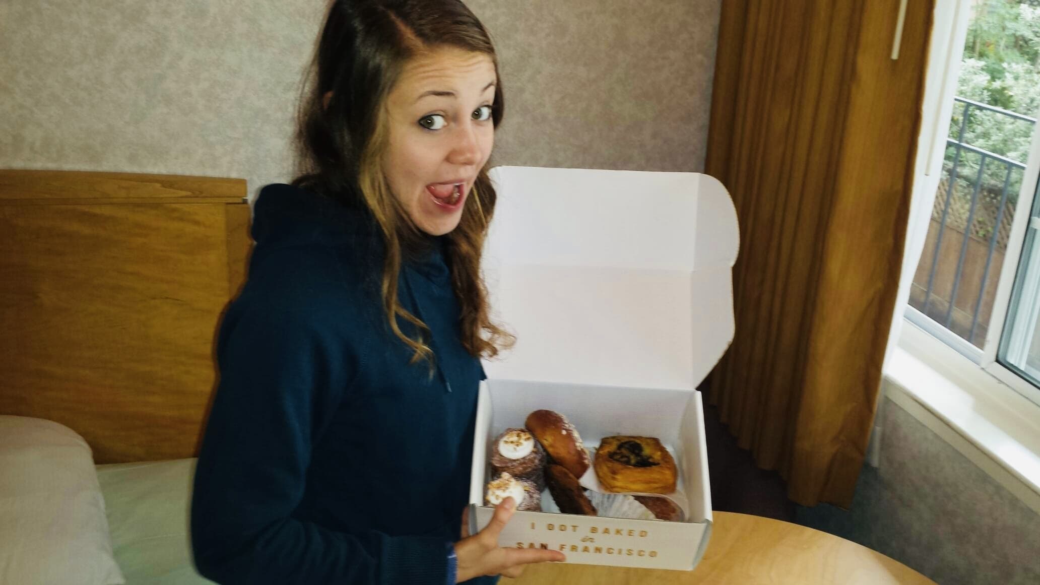 A girl holding a box of baked pastries at a circular table.
