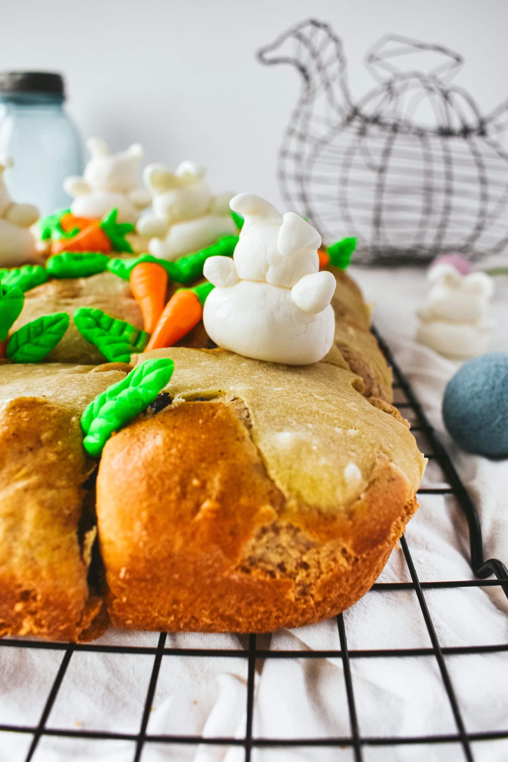 A fondant bunny and fondant carrots sitting on hot cross buns on a cooling rack. 