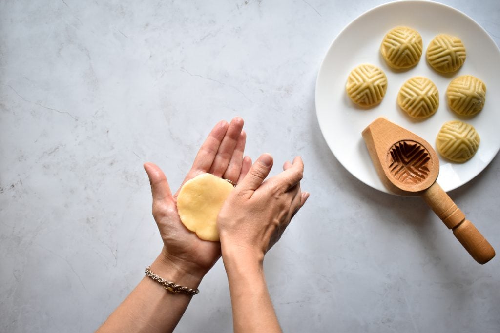 two hands pressing a disc of butter cookie dough to make ma'amoul