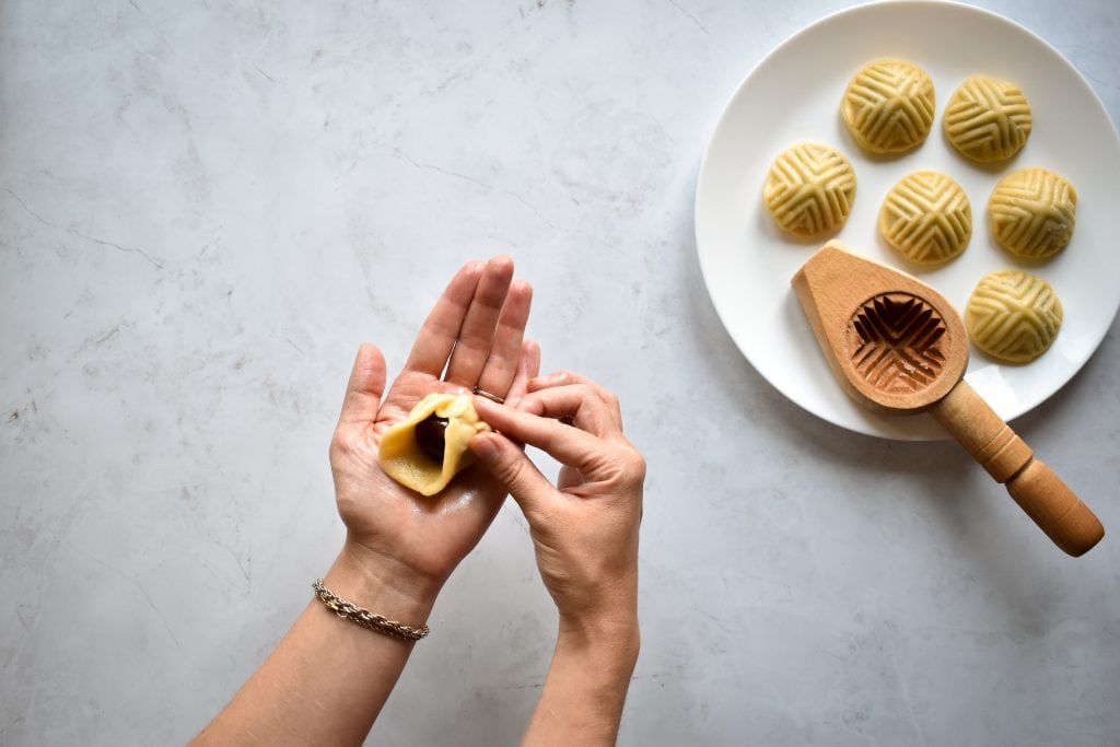 two hands forming Maamoul (Mamool) - Date Cookies next to a maamoul mold