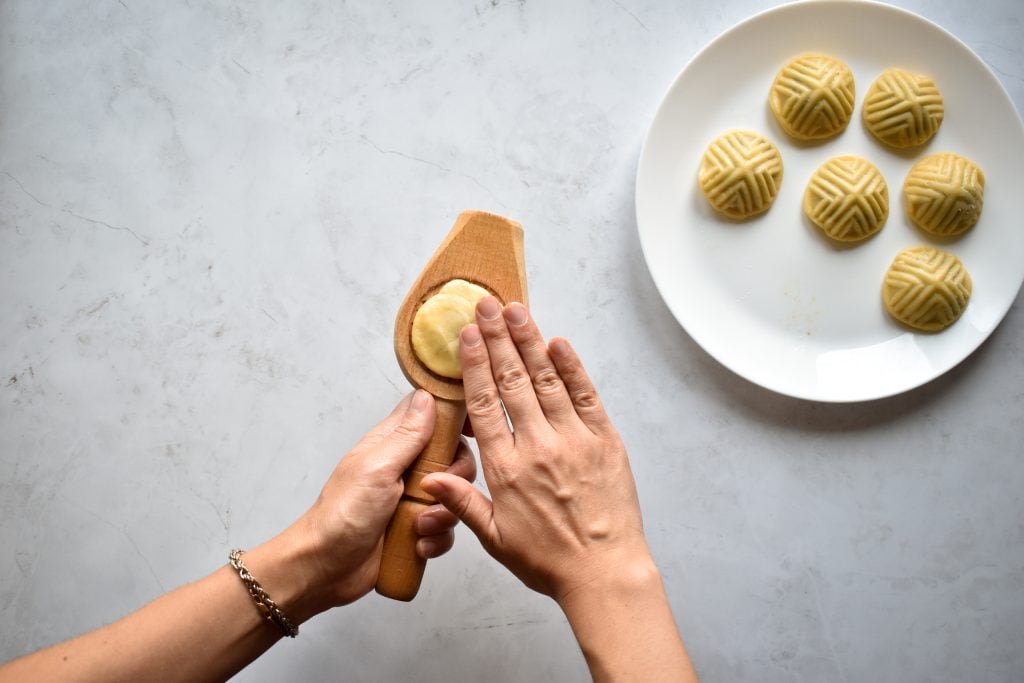 two hands pressing date cookie dough into a ma'amoul mold