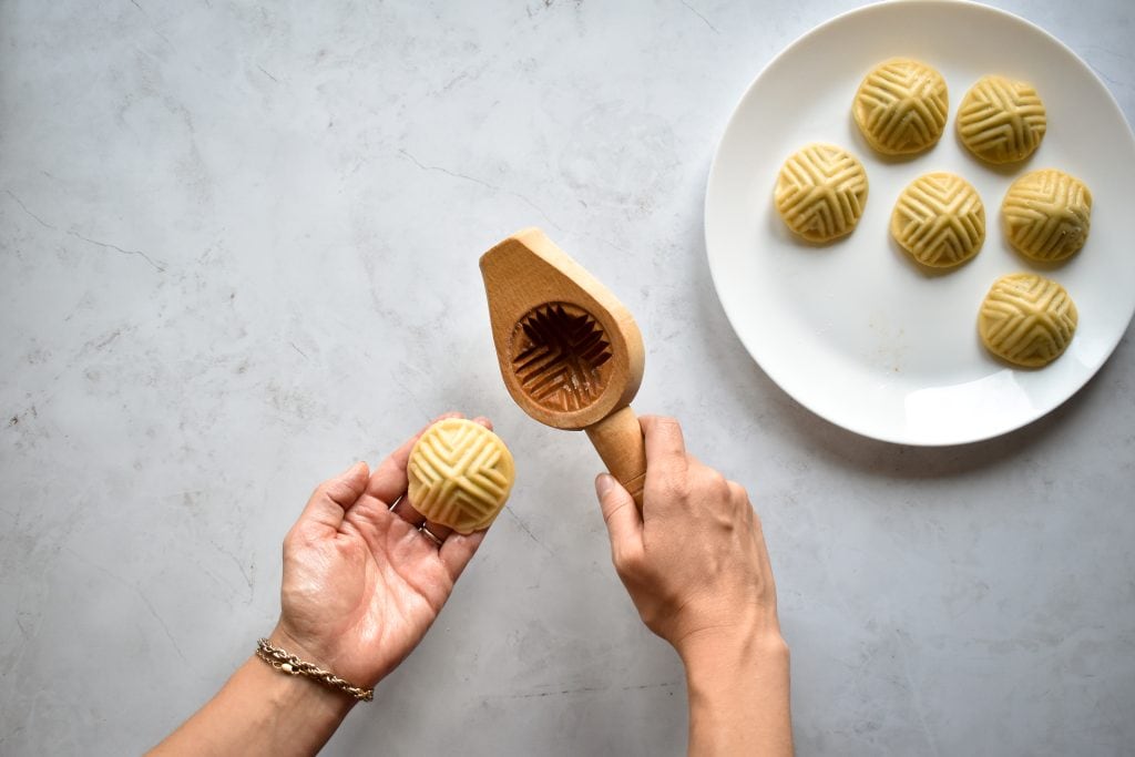 a hand holding a ma'amoul cookie mold and another hand holding a shaped ma'amoul cookie