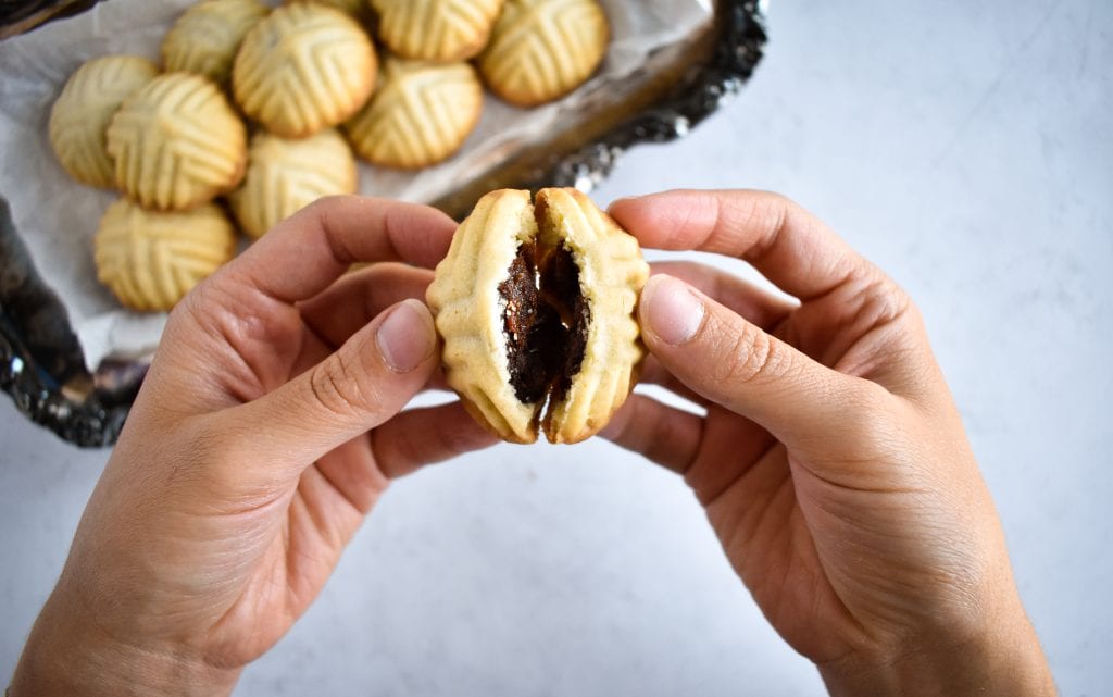 two hands pulling apart a middle eastern date cookie to show the filling inside