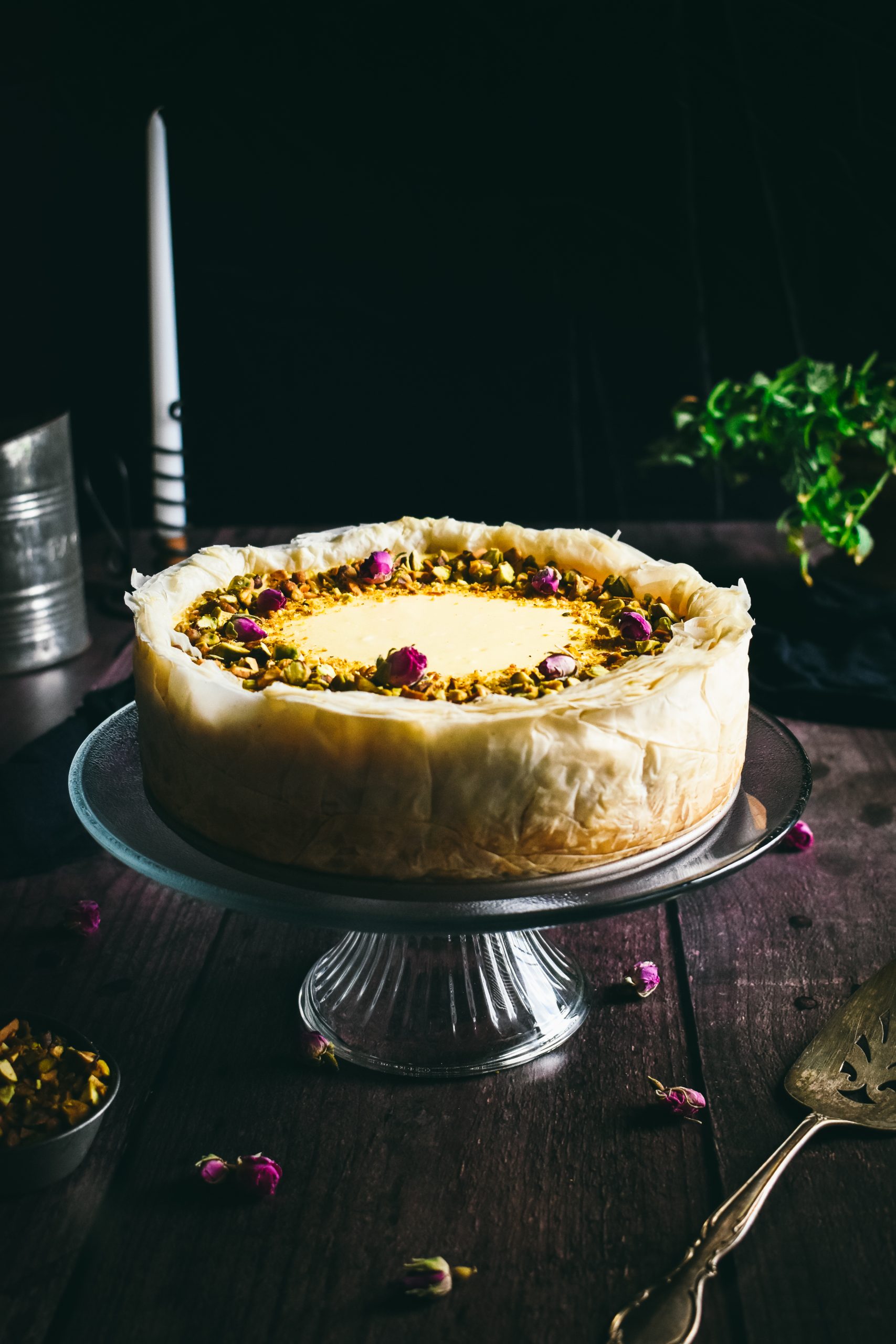 A Baklava Cheesecake on a glass cake stand in front of a black background.