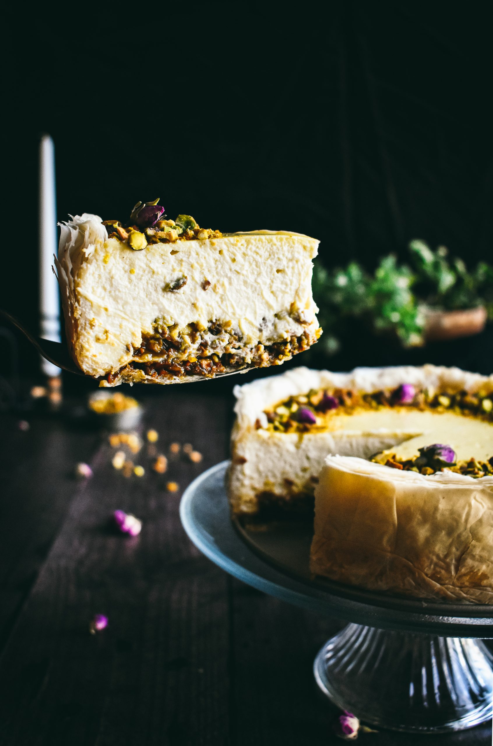 A slice of baklava cheesecake hovering near the rest of the dessert next to an unlit candle.